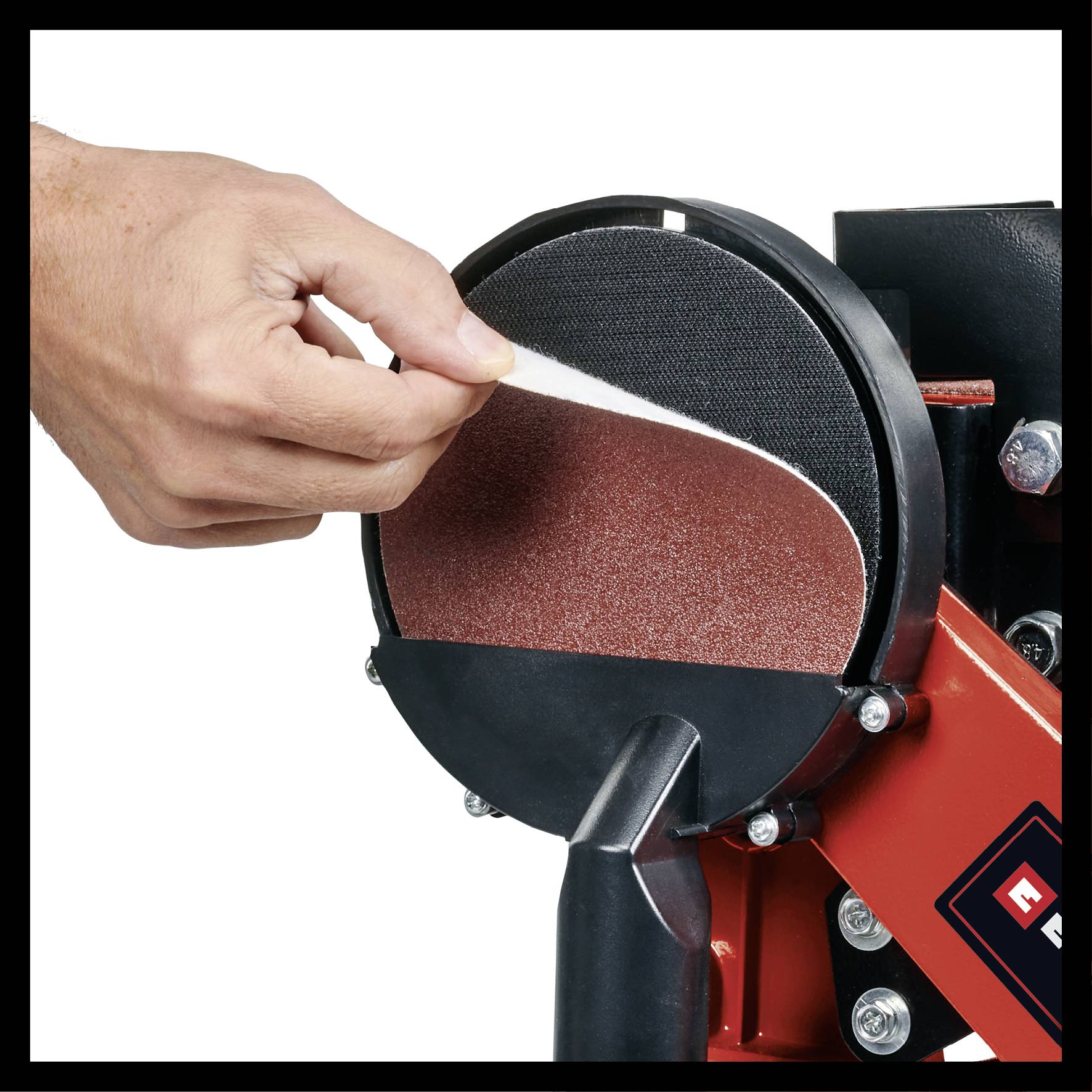 Eine Hand entfernt ein rundes Schleifpapier von einer rot-schwarzen Schleifmaschine, zeigt den Wechselvorgang.