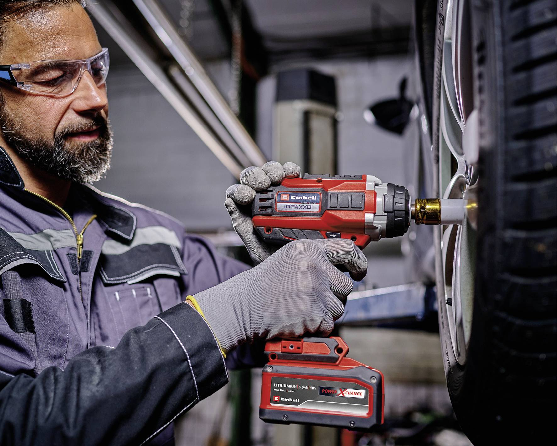 Ein Mechaniker in Sicherheitsausrüstung verwendet einen Akkuschrauber, um einen Reifen an der Felge eines Fahrzeugs in einer Werkstattumgebung zu befestigen.