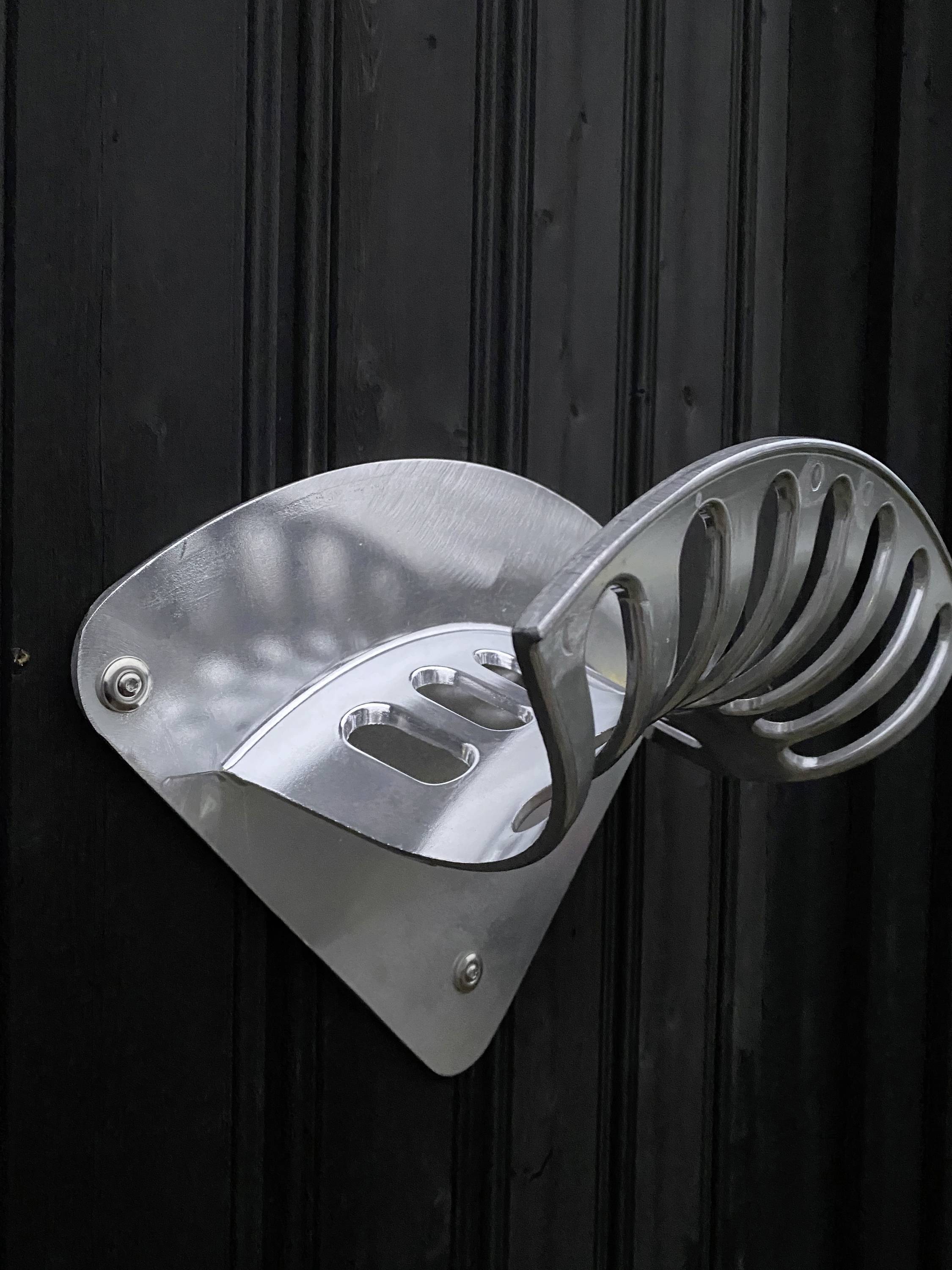 Ein silbernes, wandmontiertes, metallisches Objekt mit geschwungenem Design, wahrscheinlich ein Fahrradhalter, an schwarzer Holzverkleidung.