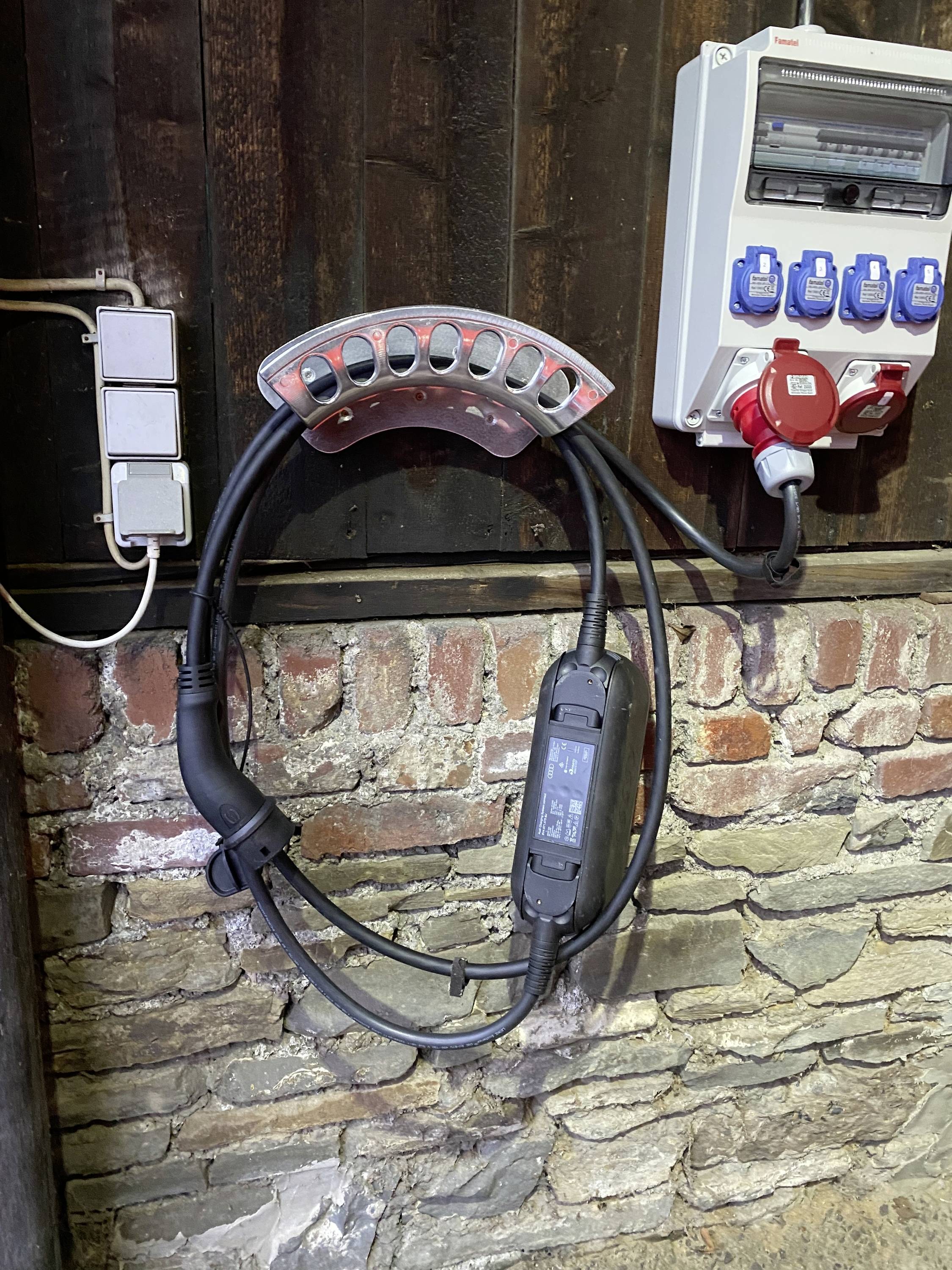 Ladestation für Elektrofahrzeuge an einer Backsteinwand; Kabel und Anschlüsse sichtbar; bereit zur Nutzung.