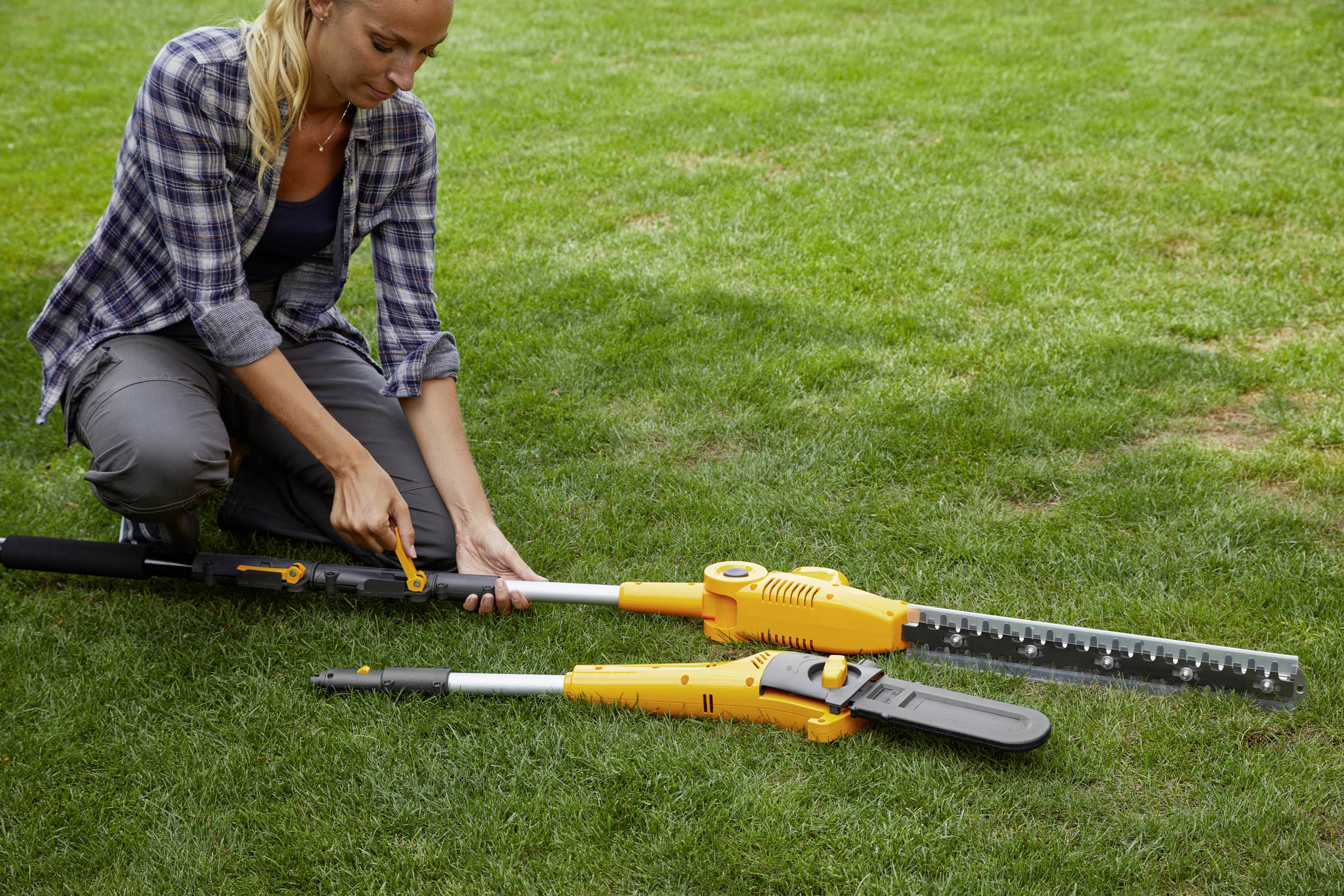Eine Person montiert ein gelbes Gartengerät auf einer Rasenfläche.