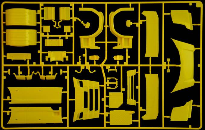 Gelber Kunststoff-Gussrahmen mit Formen von Autoteilen auf schwarzem Hintergrund, zeigt diverse Bauteile für den Zusammenbau eines Modellautos.