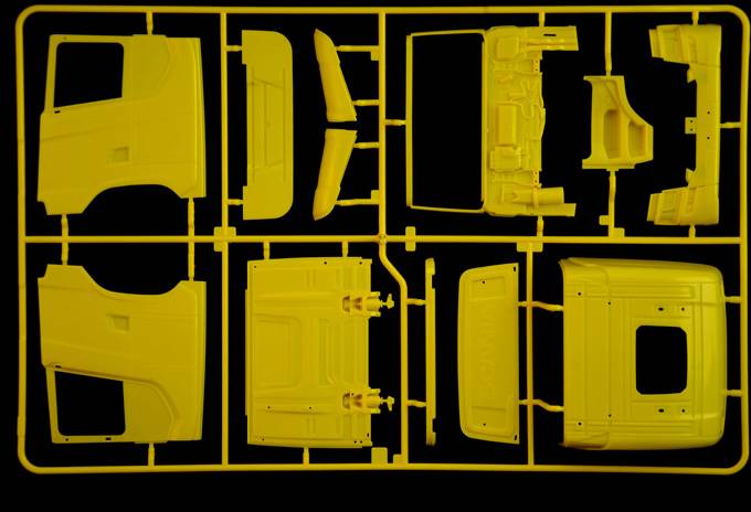 Ein gelber Kunststoffbausatz mit verschiedenen Teilen eines Modellfahrzeugs, auf einem schwarzen Hintergrund angeordnet.