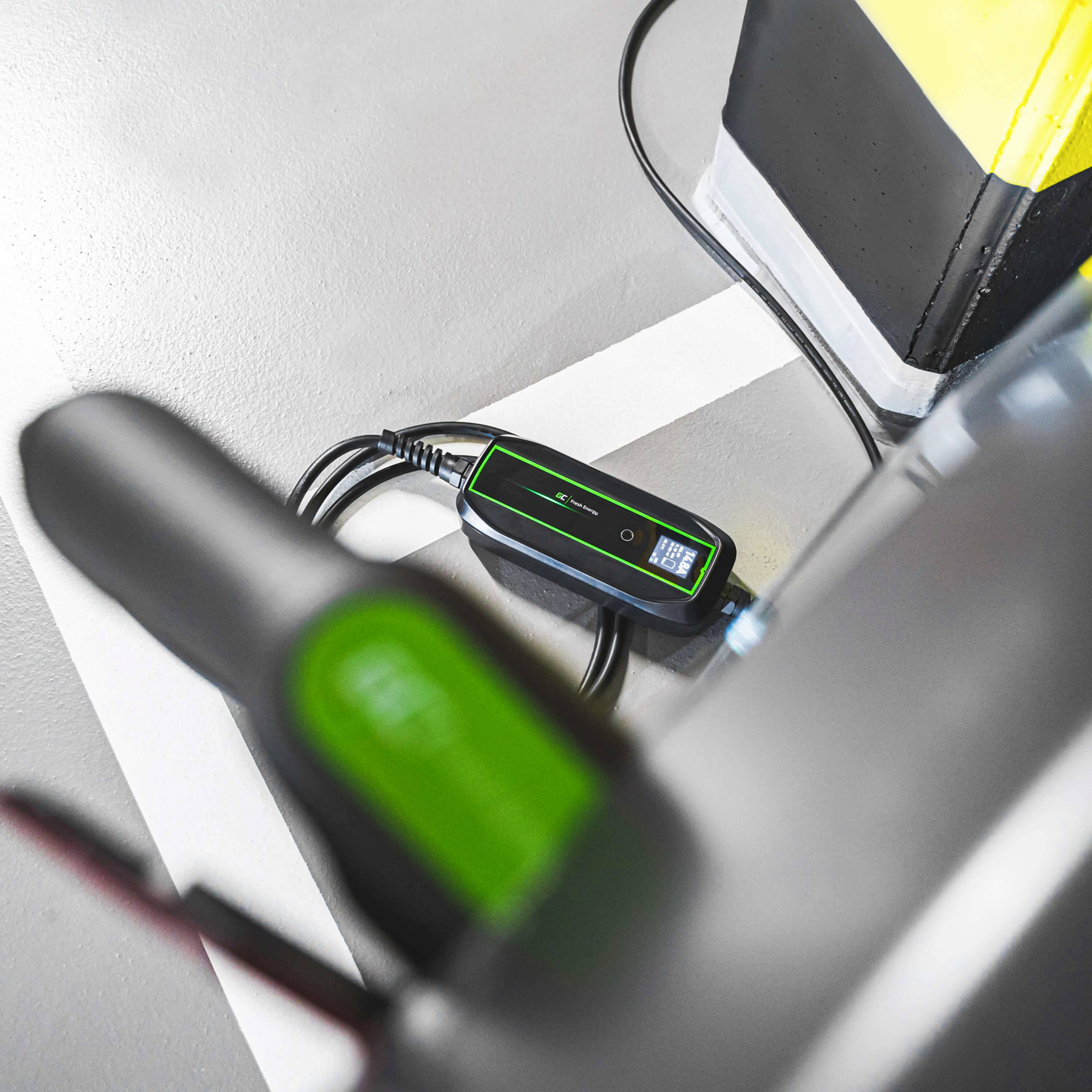 Ein E-Ladesystem ist an ein Elektrofahrzeug angeschlossen. Nahansicht des Ladegeräts auf einem grauen Boden neben einem parken Auto.