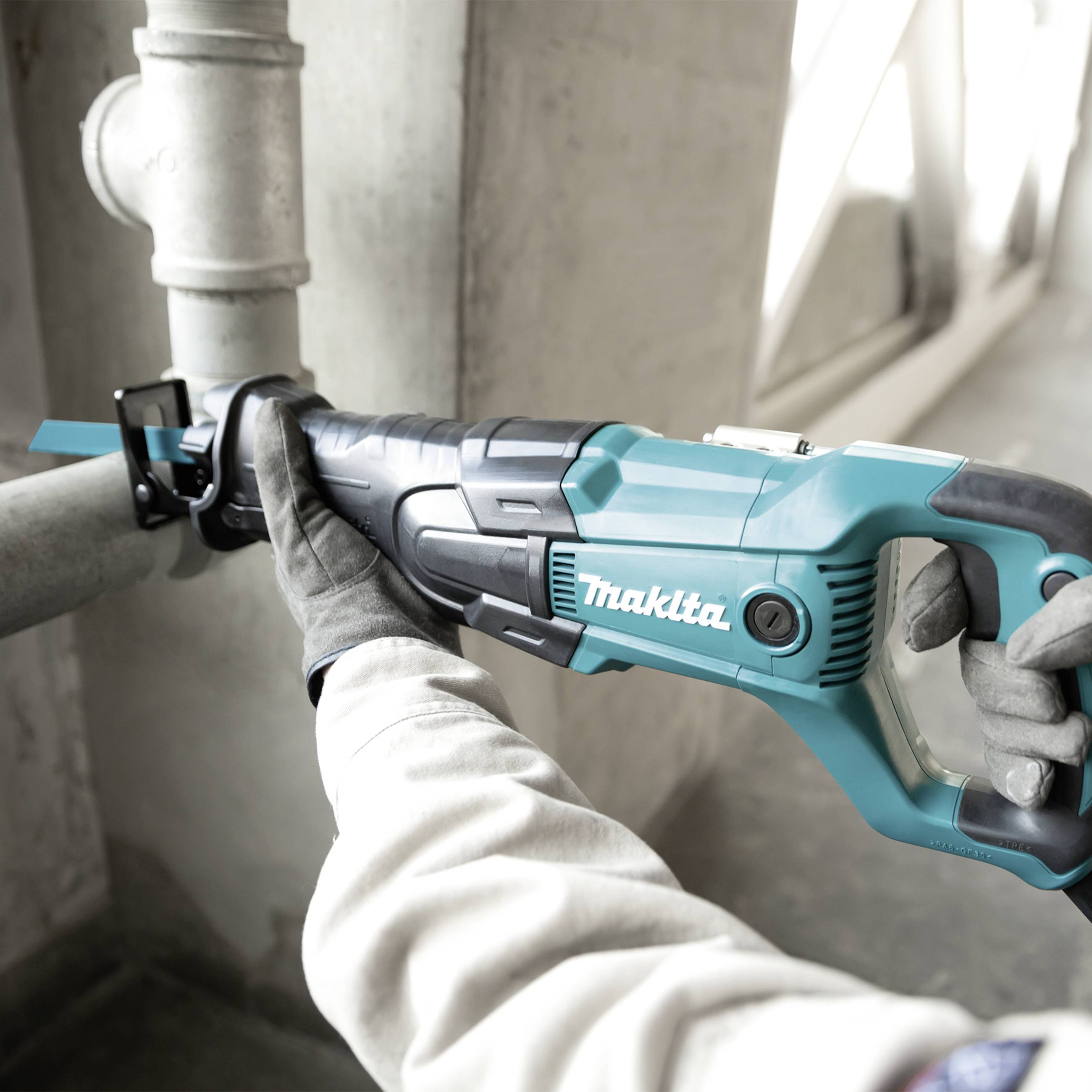 Eine Person trägt Arbeitshandschuhe und hält eine blaue elektrische Säge der Marke 'Makita', während sie ein Metallrohr schneidet.