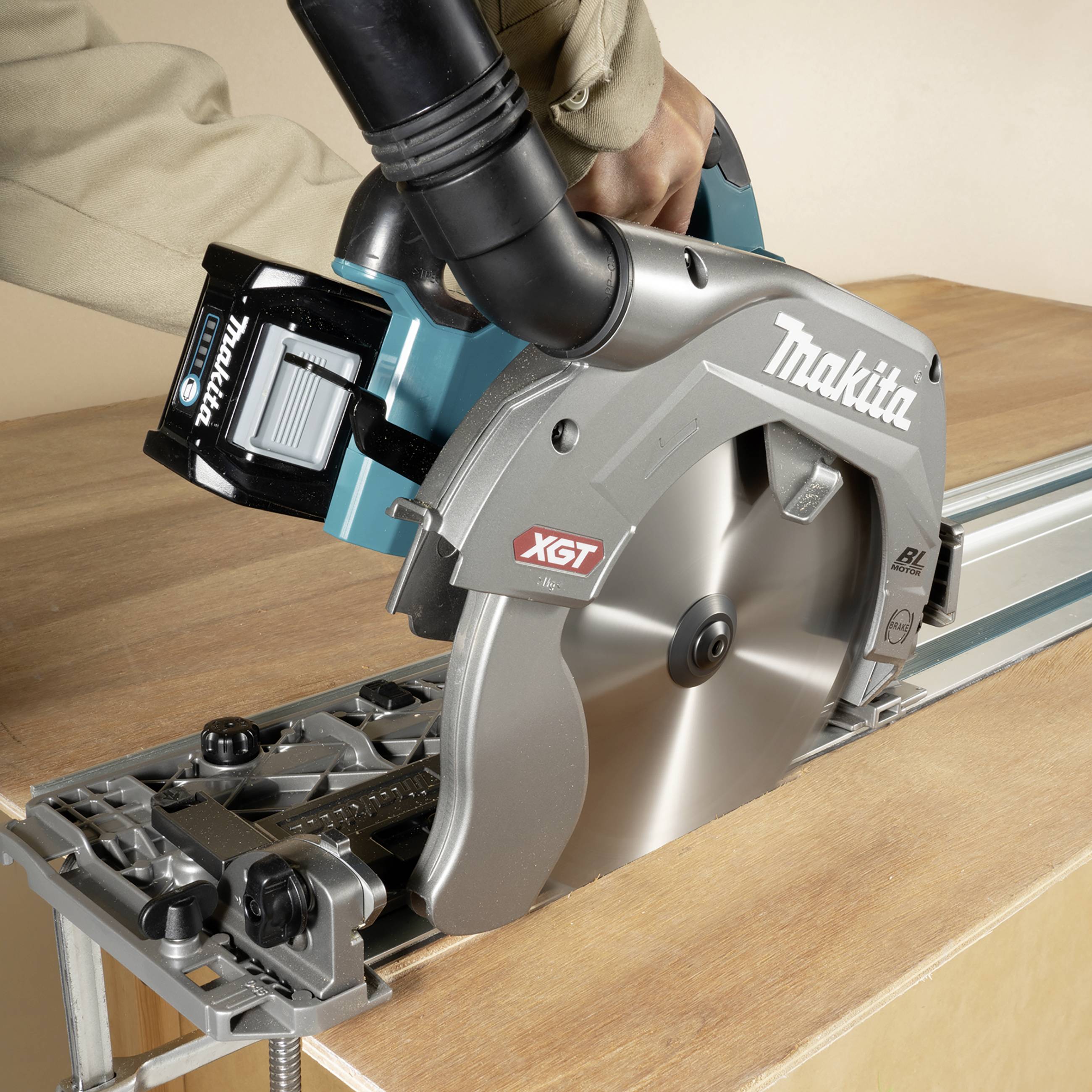Eine Person bedient eine Makita Kreissäge, die an einer Holzplatte arbeitet. Die Säge ist mit einer Führungsschiene für präzise Schnitte ausgestattet.