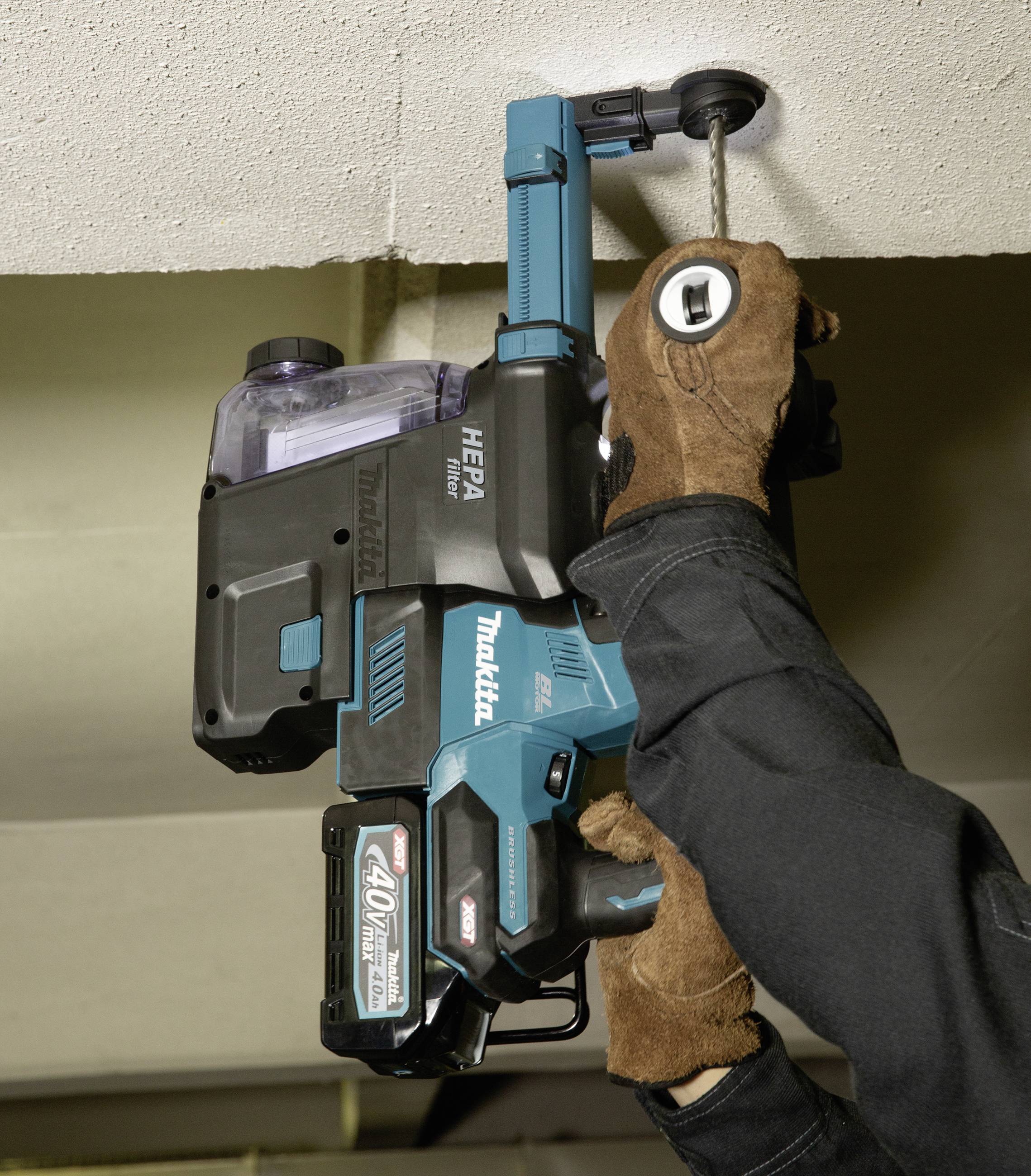 Arbeiter nutzt eine blaue, elektrische Bohrmaschine, um ein Loch in eine Decke zu bohren. Er trägt braune Handschuhe für Schutz.