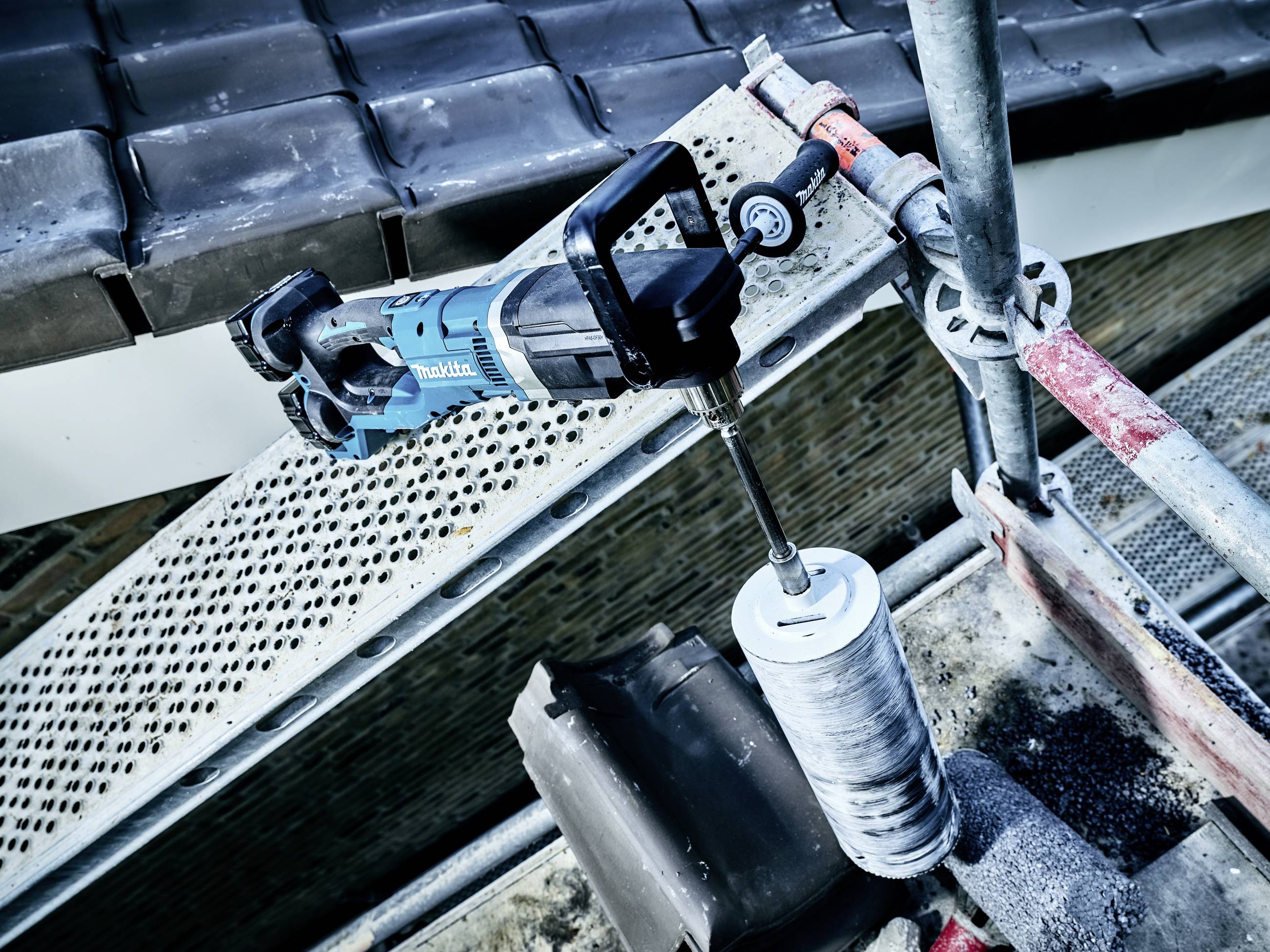Eine blaue Bohrmaschine befindet sich auf einem Baugerüst. Sie ist mit einem großen Bohrer ausgestattet, geeignet für Maurerarbeiten.
