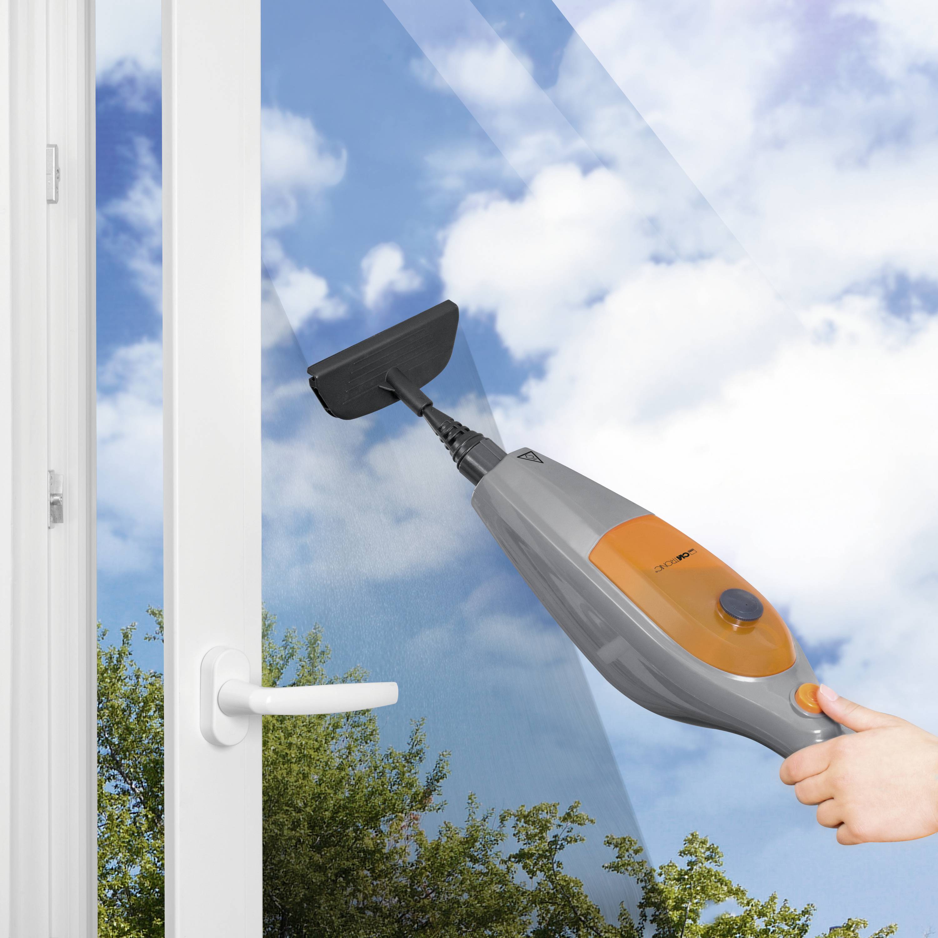 Eine Hand hält einen Dampfreiniger und reinigt ein großes Fensterglas mit wolkenfreiem Himmel und Bäumen im Hintergrund.