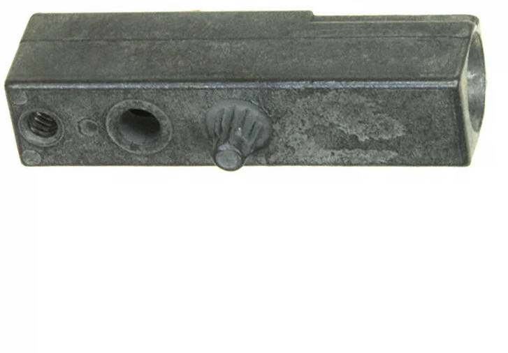 Ein grauer Metallblock mit mehreren kreisförmigen Öffnungen und einem kleinen zahnradähnlichen Knopf in der Mitte, möglicherweise Teil einer mechanischen Komponente.