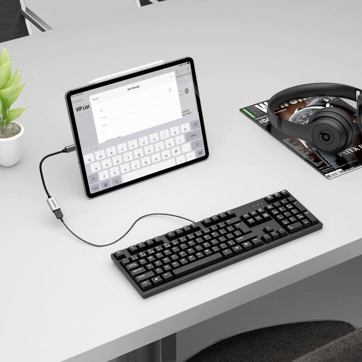 Ein Tablet mit angezeigter Tastatur ist über ein Kabel mit einer physischen Tastatur verbunden. Daneben liegt ein Kopfhörer auf einer Zeitschrift.