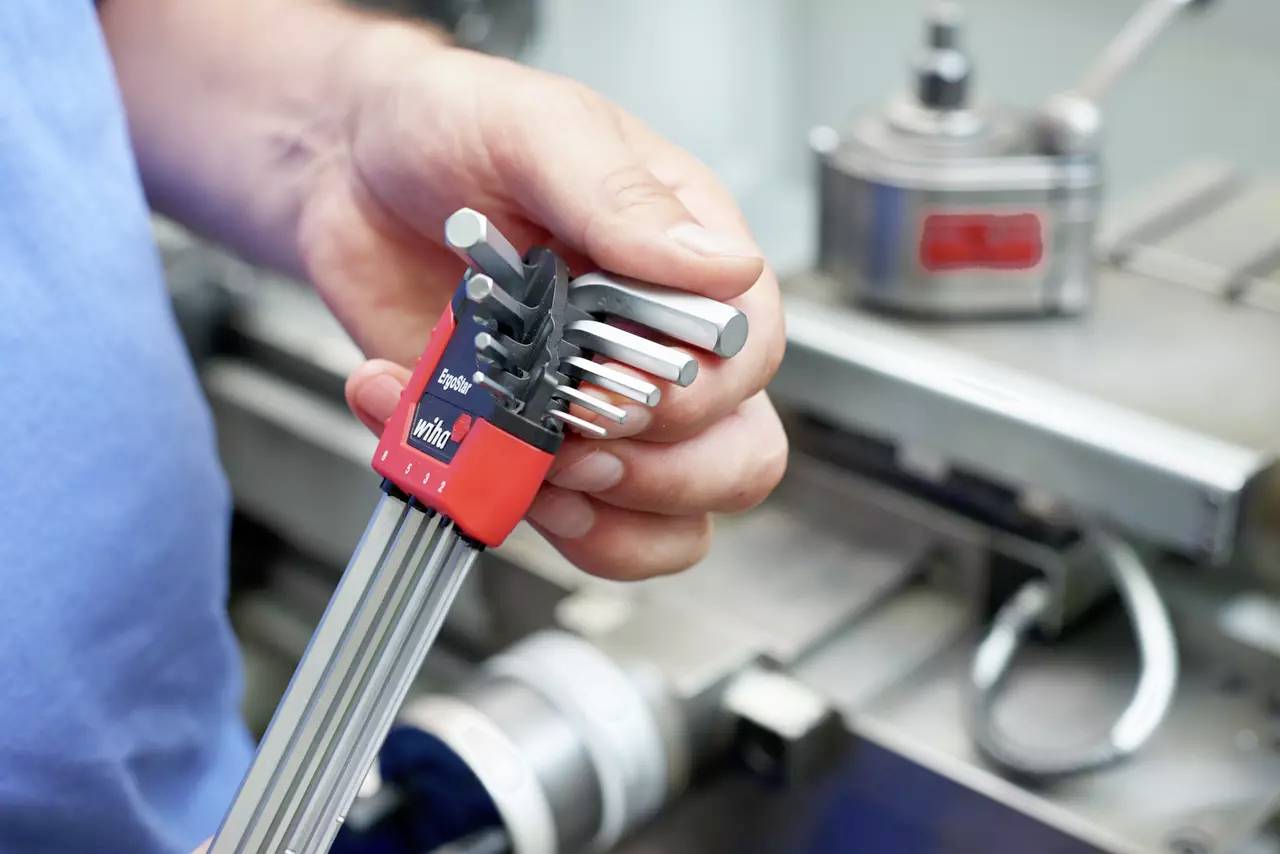 Eine Person hält einen Satz Inbusschlüssel in einer Werkstatt. Die Metallwerkzeuge sind organisiert und decken verschiedene Größen ab, was auf ihre Vielseitigkeit in der Anwendung hinweist.