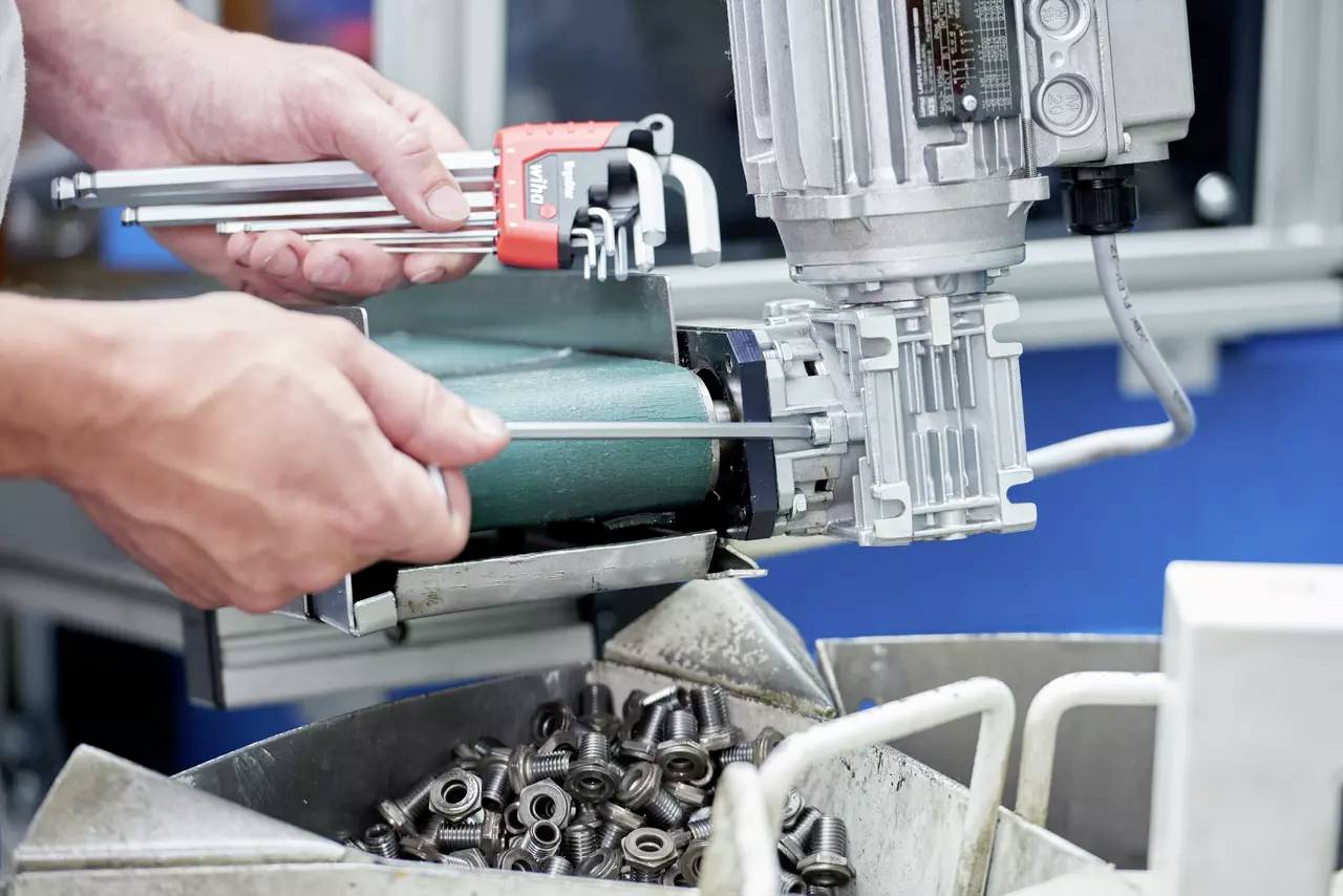 Eine Person verwendet ein Werkzeug zur Messung von Komponenten in einer Maschinenumgebung, wobei Metallteile darunter gesammelt werden und einen Fertigungsprozess andeuten.