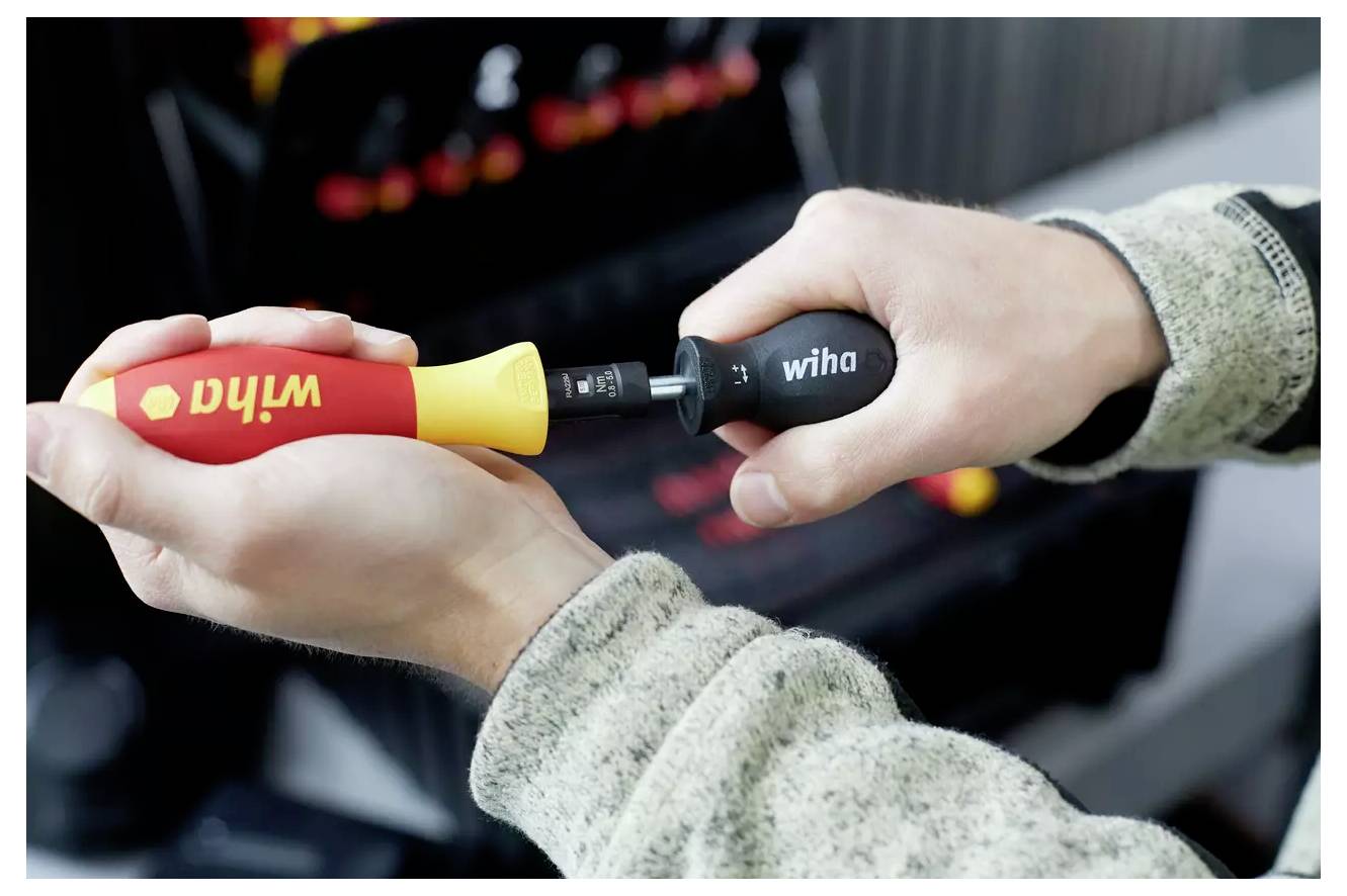 Zwei Hände halten einen Mehrbit-Schraubendreher. Eine Hand greift den Griff mit der Aufschrift „Wiha