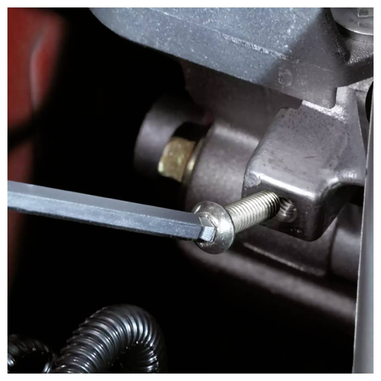 Eine Nahaufnahme eines Motorenteils mit einem Handwerkzeug, das eine Schraube verstellt, was eine laufende Wartung oder Reparatur zeigt.