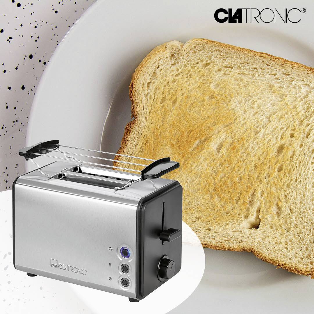 Ein silberner Toaster mit zwei Schlitzen, daneben eine Scheibe getoastetes Brot. Im Hintergrund ein schwarz-weiß gesprenkelter Hintergrund.