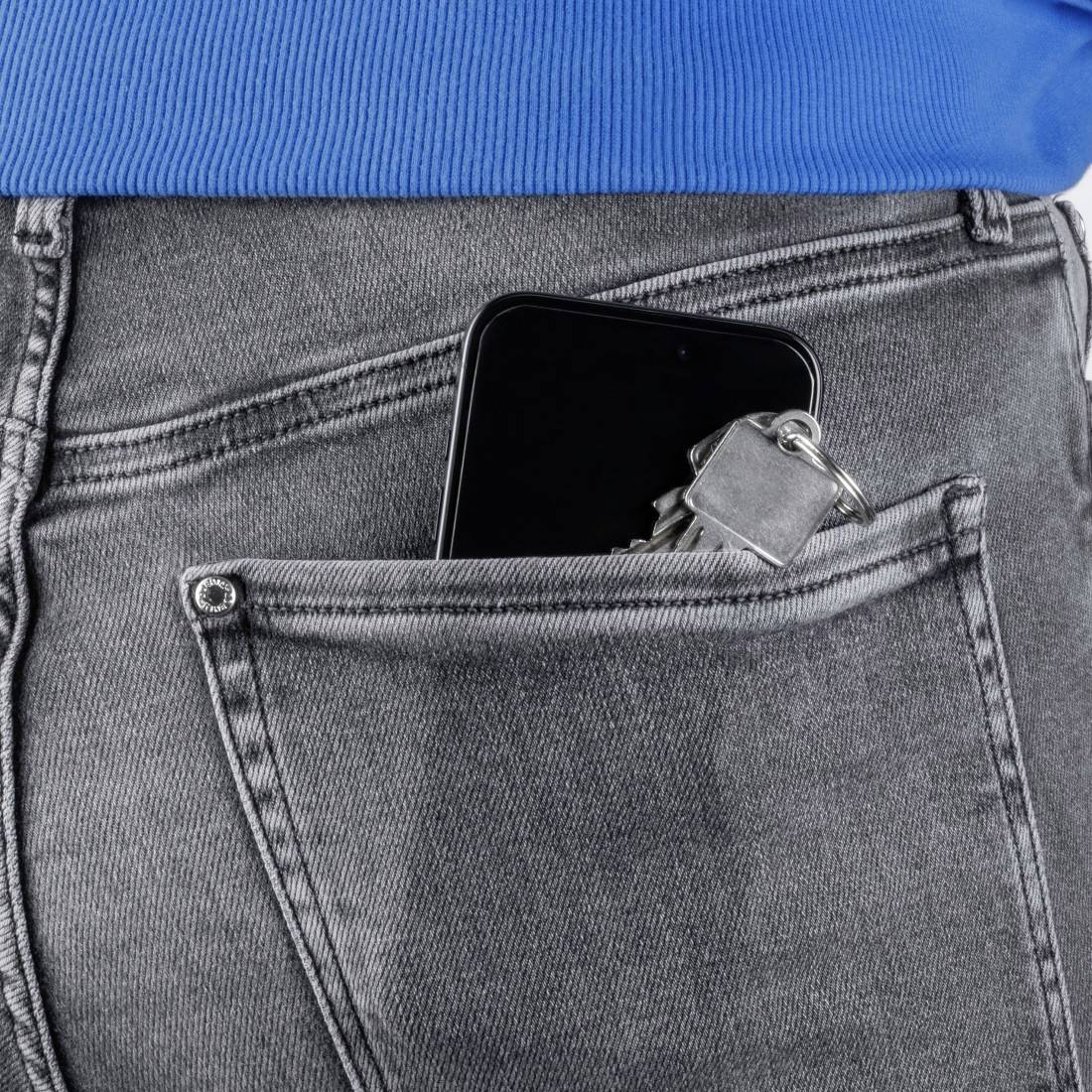 Eine Person trägt eine blaue Jacke. Ein Smartphone und ein Schlüsselbund stecken sichtbar in der Gesäßtasche einer grauen Jeans.
