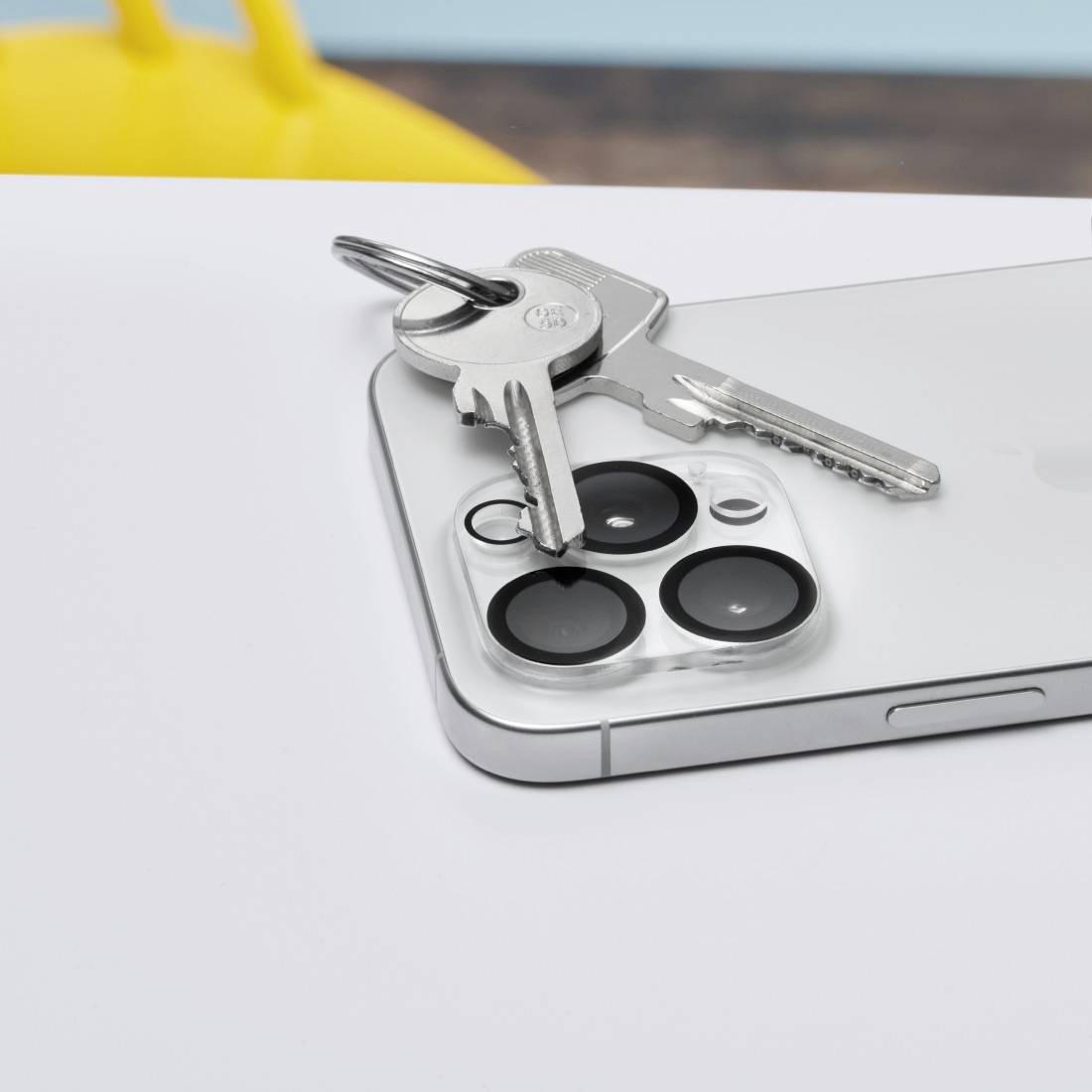 iPhone mit drei Kameralinsen auf einem Tisch, auf dem Schlüssel liegen. Fokus liegt auf den Kameralinsen.