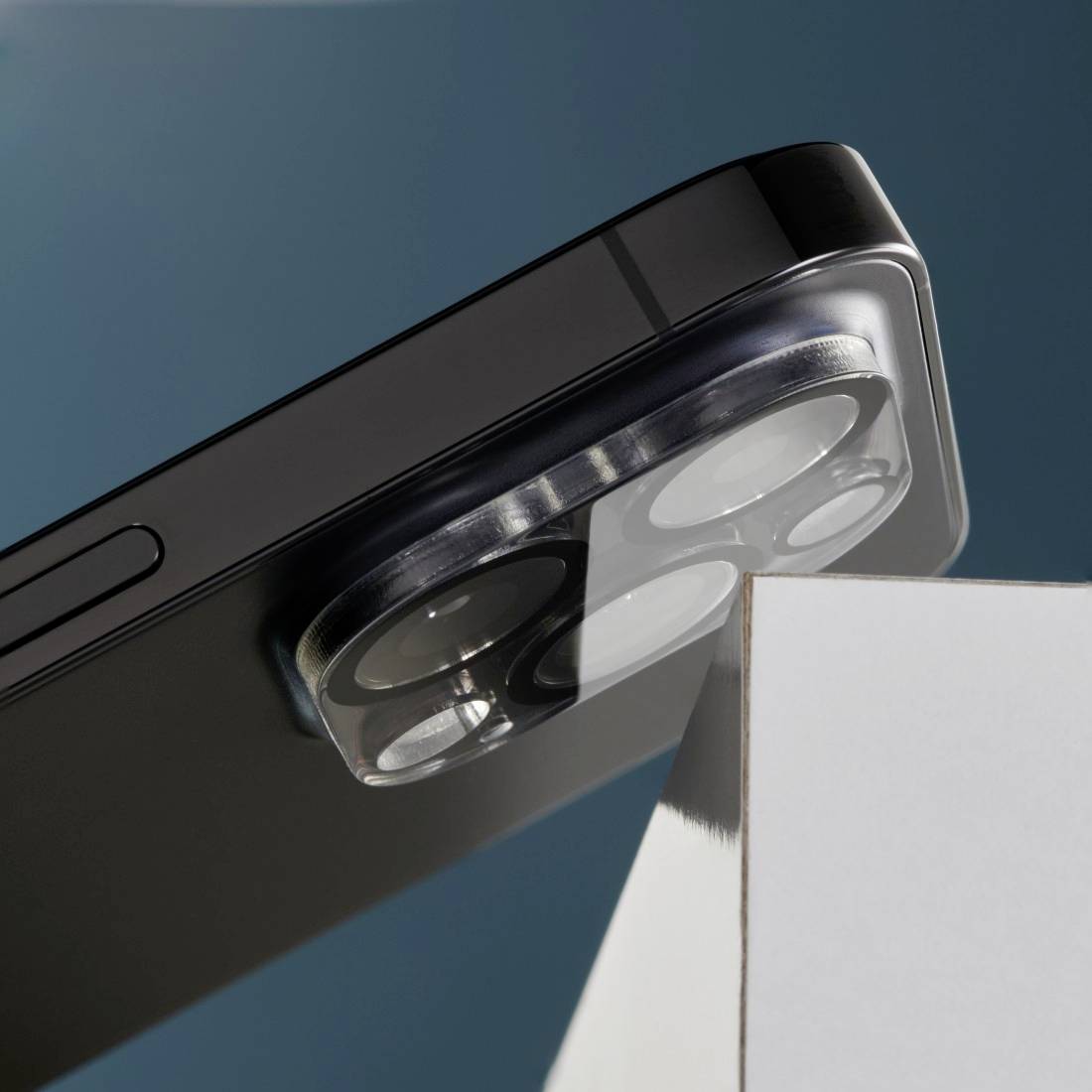 Nahaufnahme eines Smartphones mit hervorstehendem Kameramodul. Das Gerät liegt auf einer weißen Kante vor blauem Hintergrund.