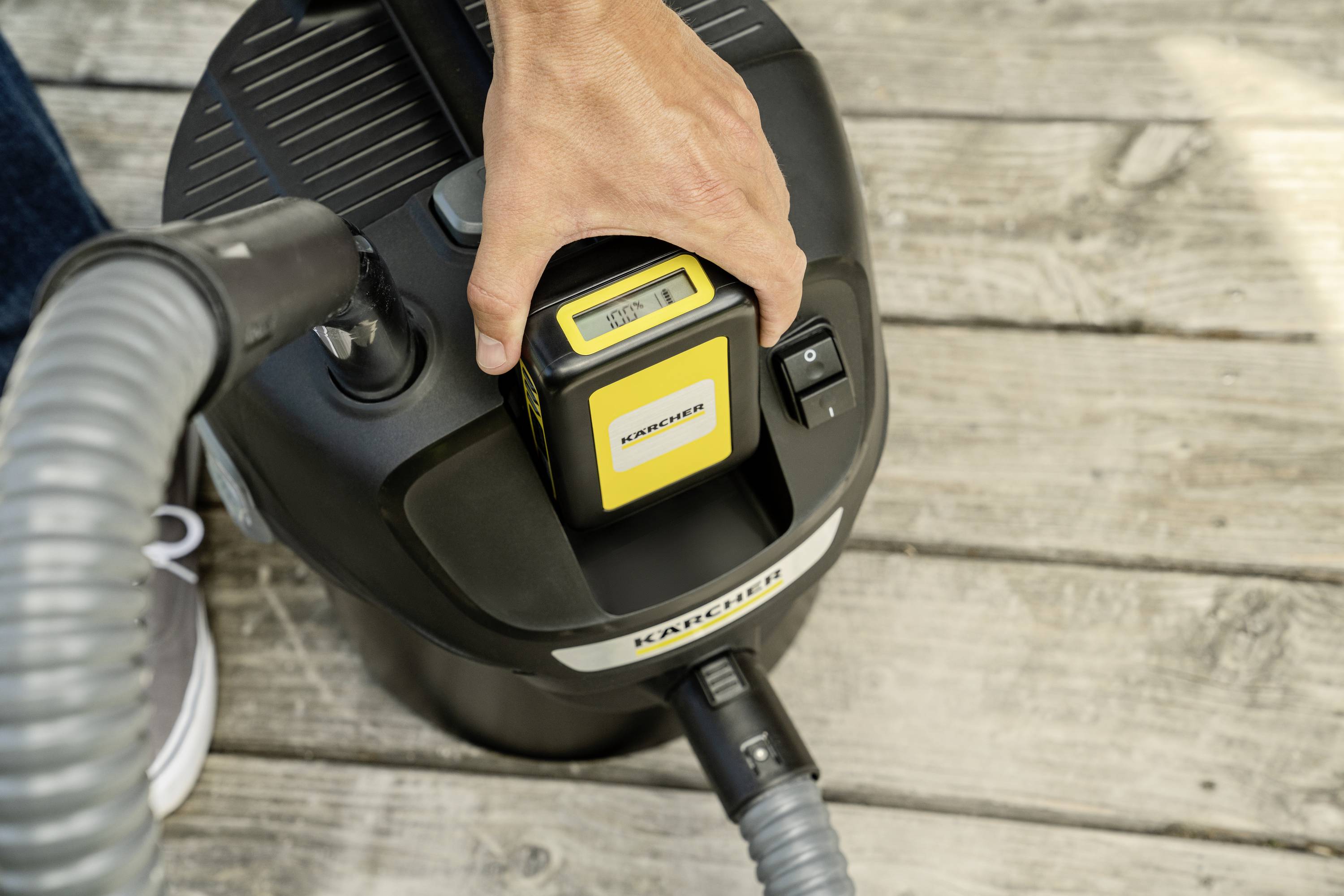 Eine Person setzt einen Akku in einen tragbaren Staubsauger ein, der auf einem Holzboden steht.