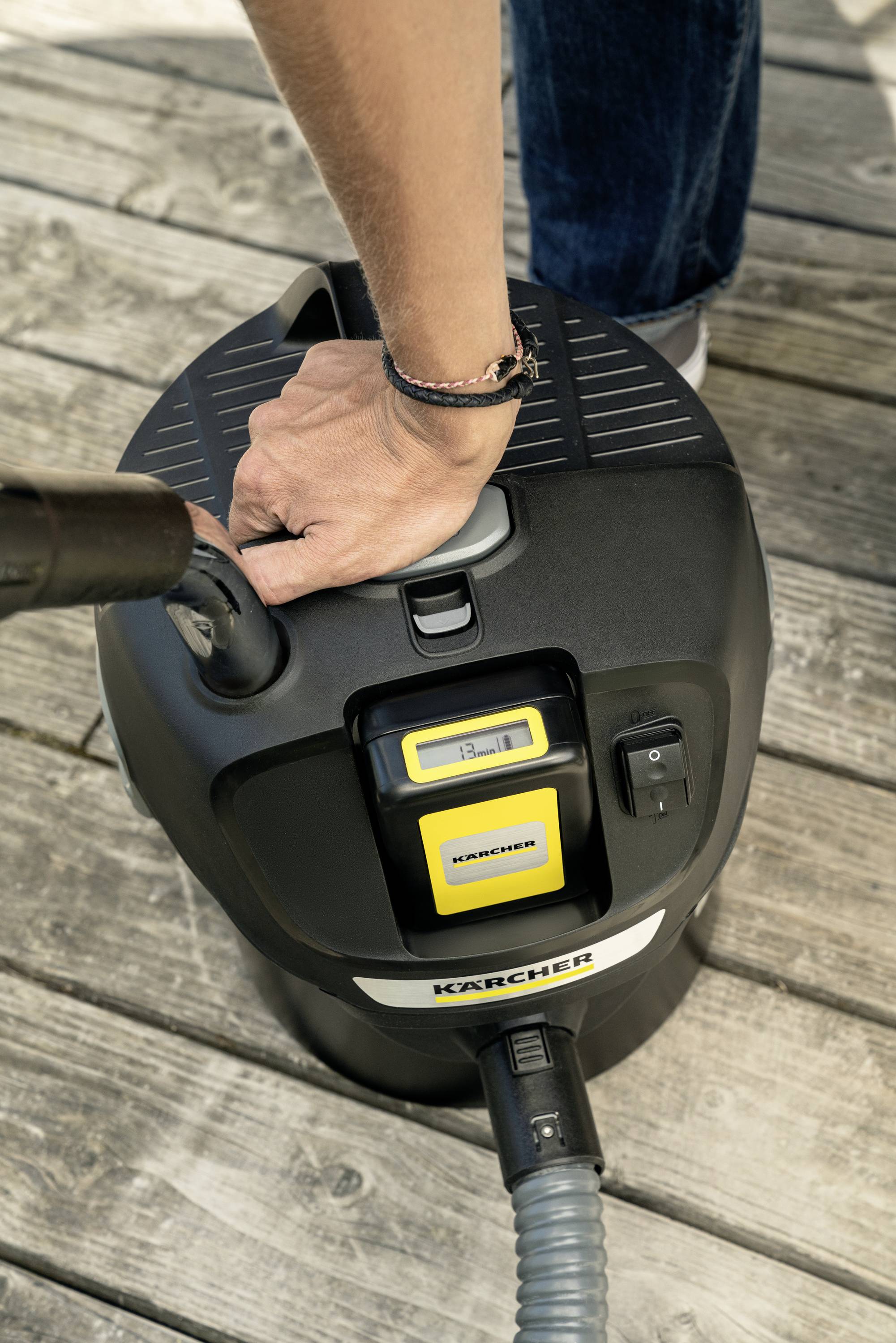 Person reinigt Holzterrasse mit einem Nass-/Trockensauger. Hand hält den Griff des Geräts. Gerät steht auf der Terrasse.