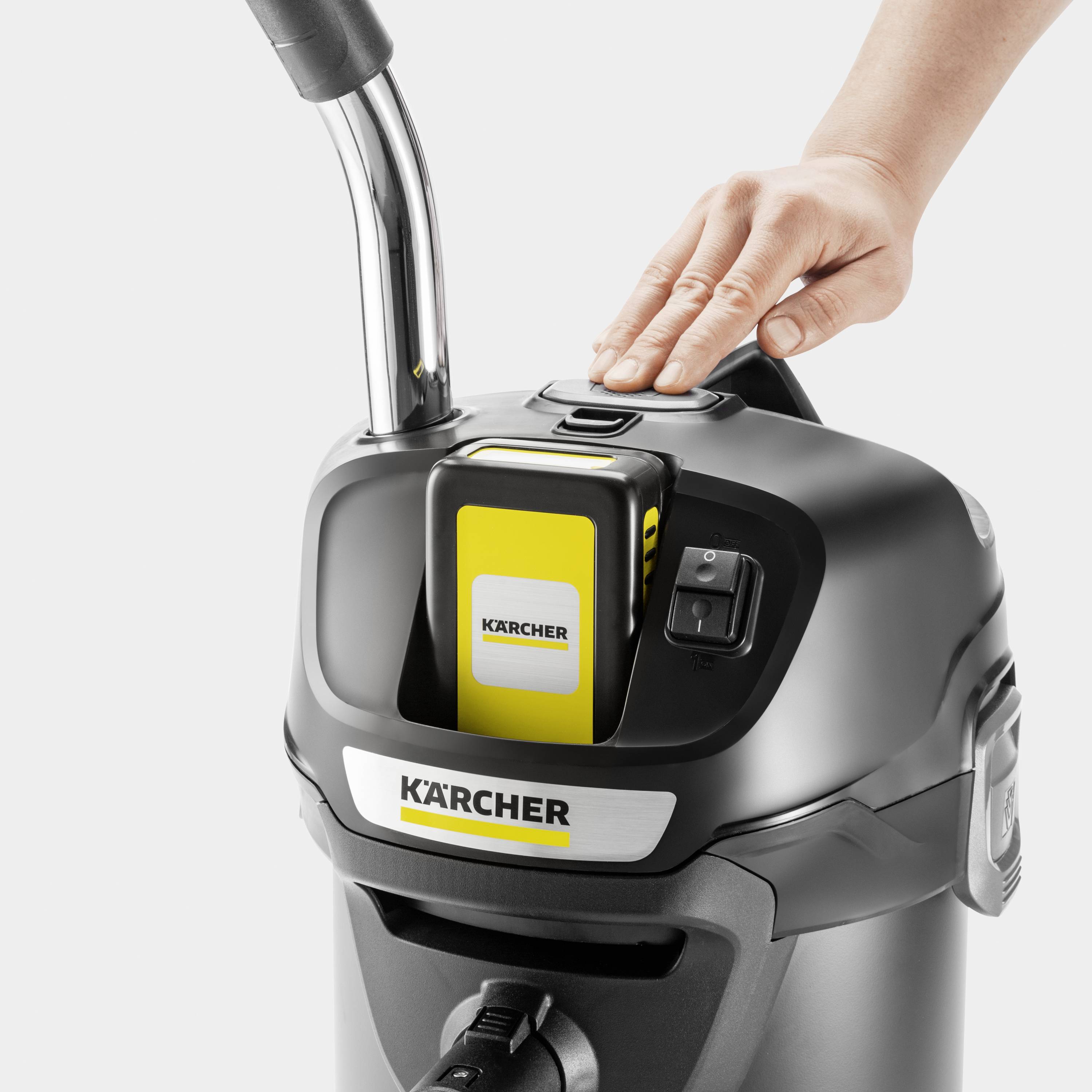 Hand, die eine gelbe Karcher-Reinigungsmaschine am Bedienfeld betätigt. Gerät mit ergonomischem Griff, silber-schwarzem Design.