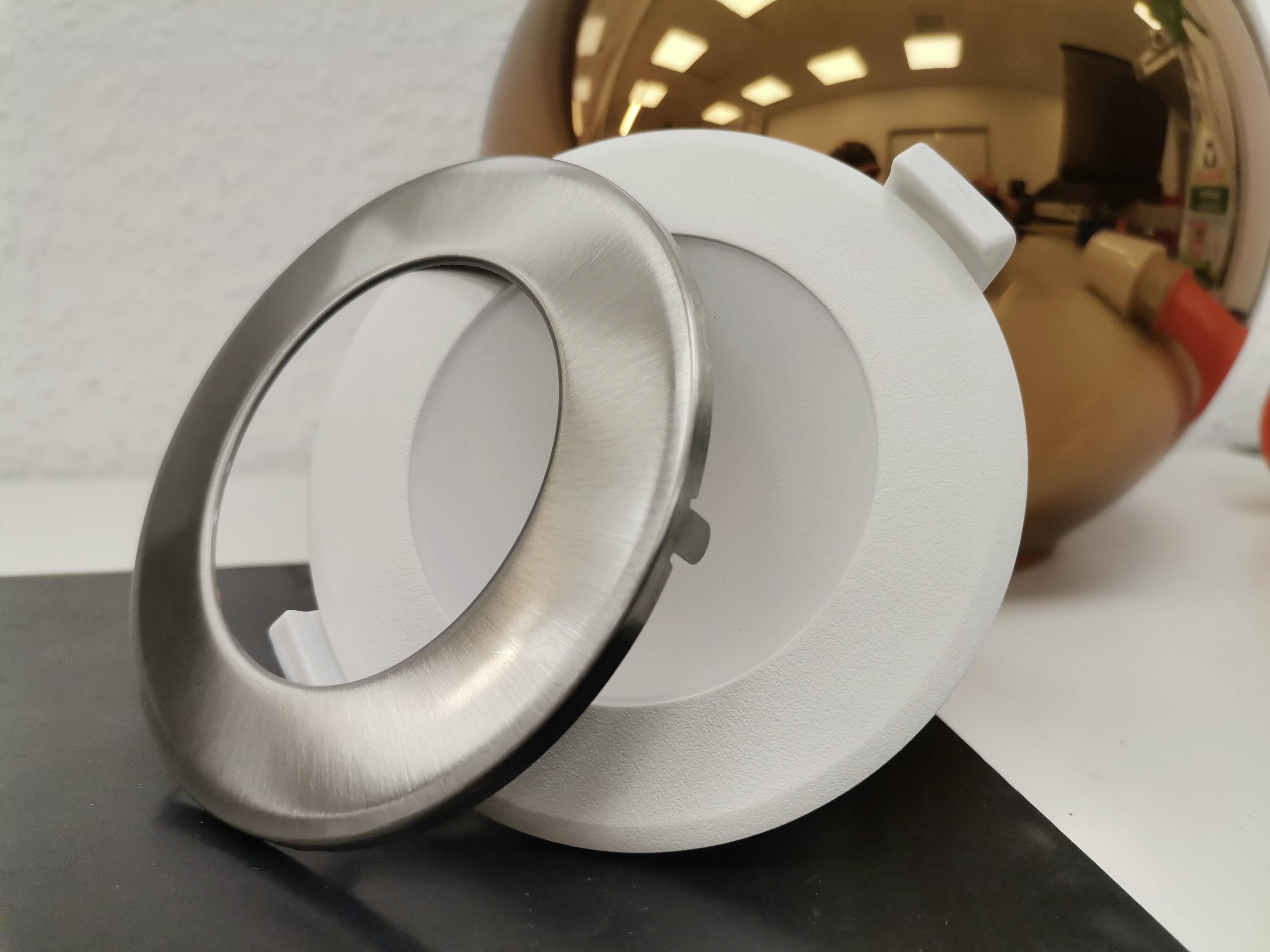 Zwei runde Abdeckungen, eine aus silbernem Metall und eine aus weißem Kunststoff, liegen auf einem Tisch nebeneinander.