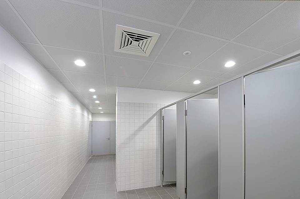 Ein steriler, moderner Toilettenraum mit weißen Fliesen, mehreren geschlossenen Kabinentüren und heller Deckenbeleuchtung.