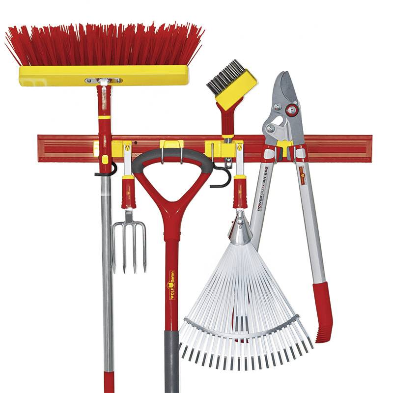 Verschiedene Gartenwerkzeuge: Rechen, Besen, Astschere, Handharke und Fugenbürste sind an einer Wandhalterung organisiert angeordnet.
