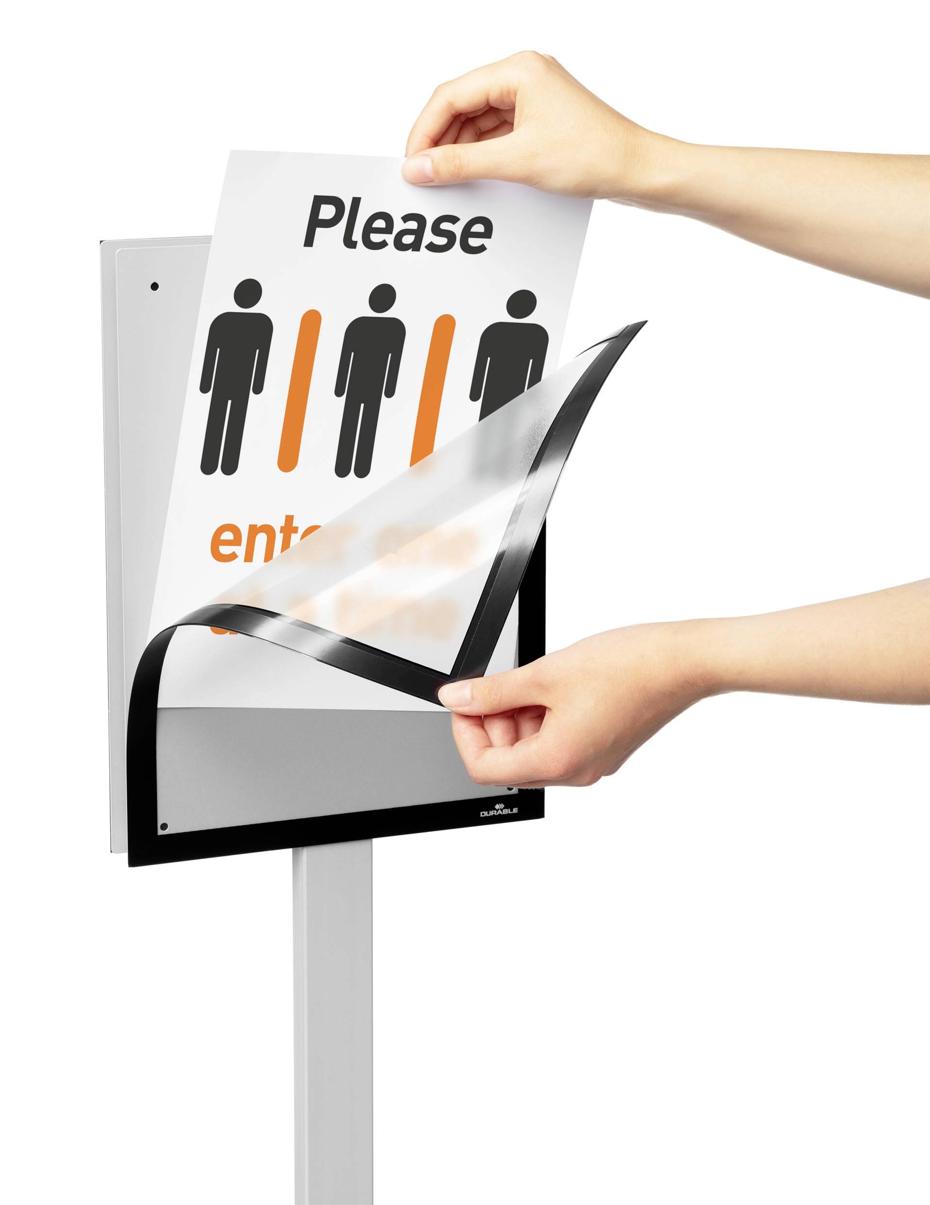 Eine Person wechselt ein Schild mit der Aufschrift 'Please enter' und Piktogrammen von Menschen. Es zeigt den Austausch von Informationen.