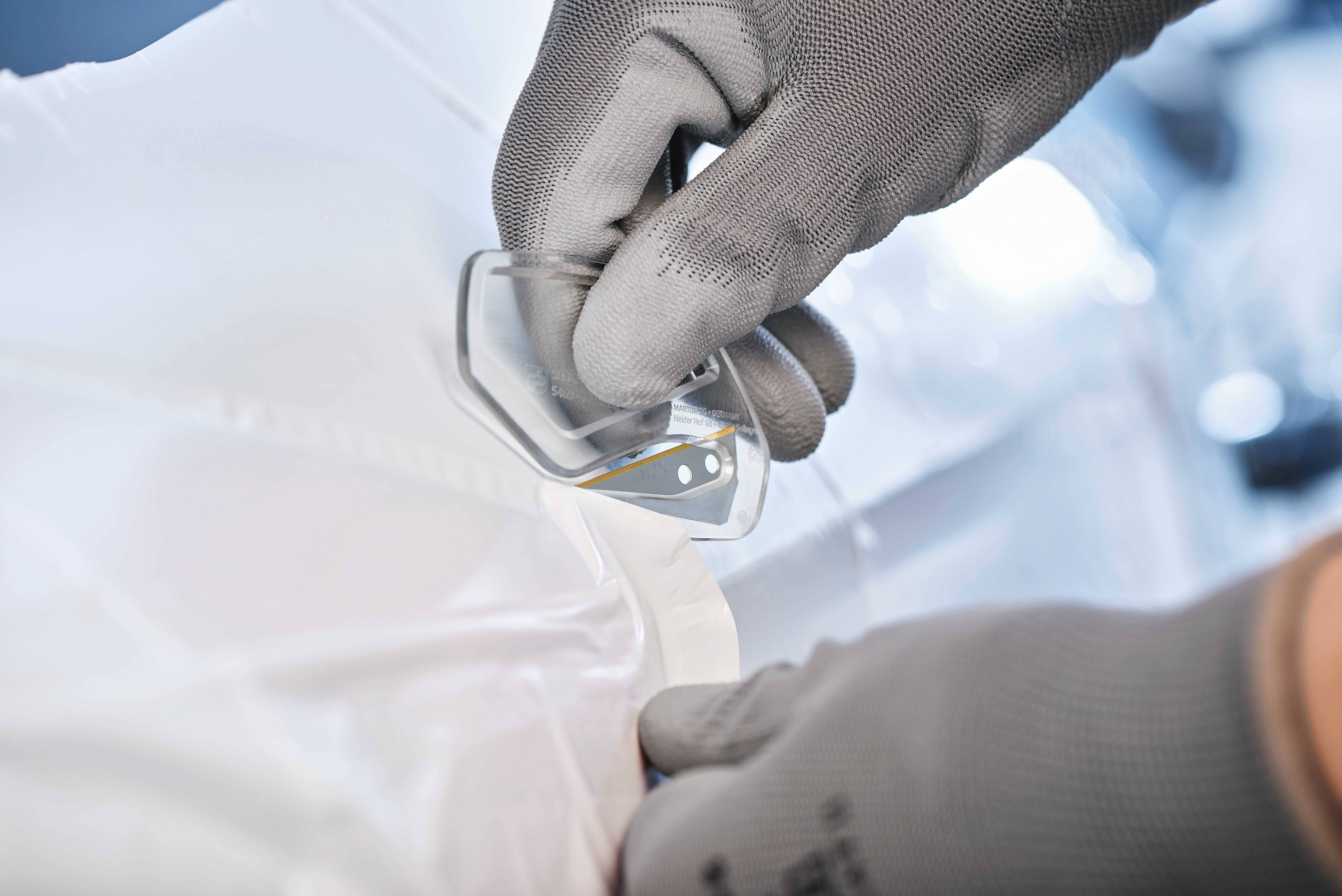 Eine Person mit grauen Handschuhen befestigt einen kleinen transparenten Sensor an einem weißen, weichen Material.