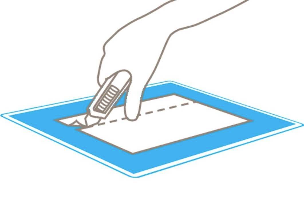 Eine Hand benutzt einen Cutter, um entlang einer gestrichelten Linie auf einem blauen Rechteck zu schneiden.
