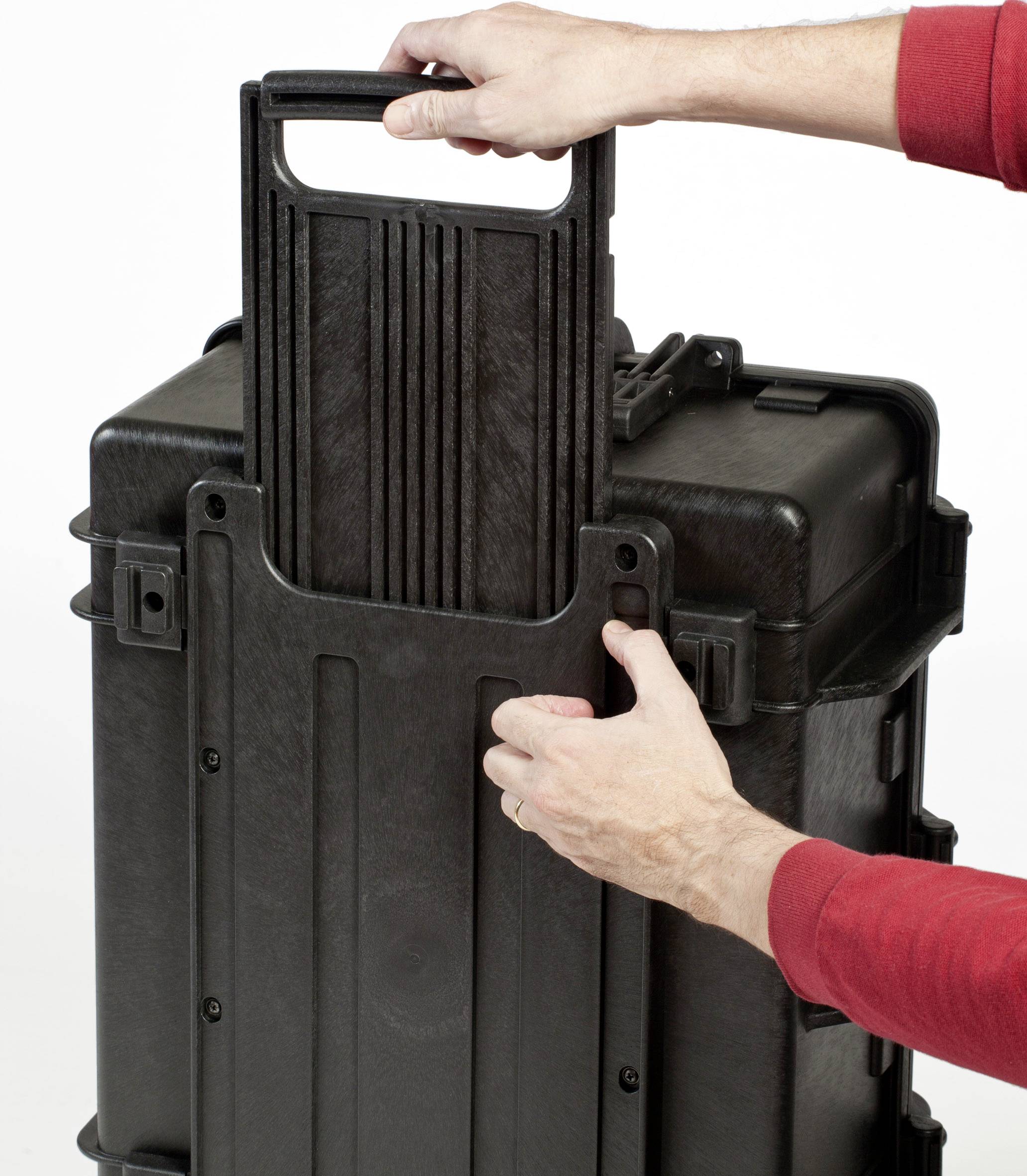Eine Person zieht den Griff eines großen, schwarzen, robusten Transportkoffers heraus.