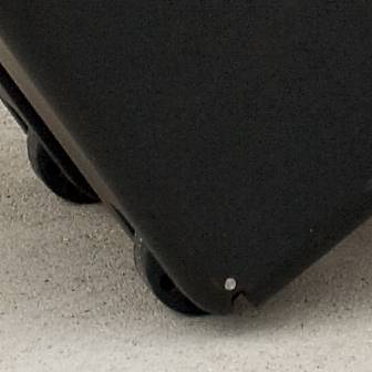 Ein Teil eines schwarzen Rollkoffers auf sandigem Boden.