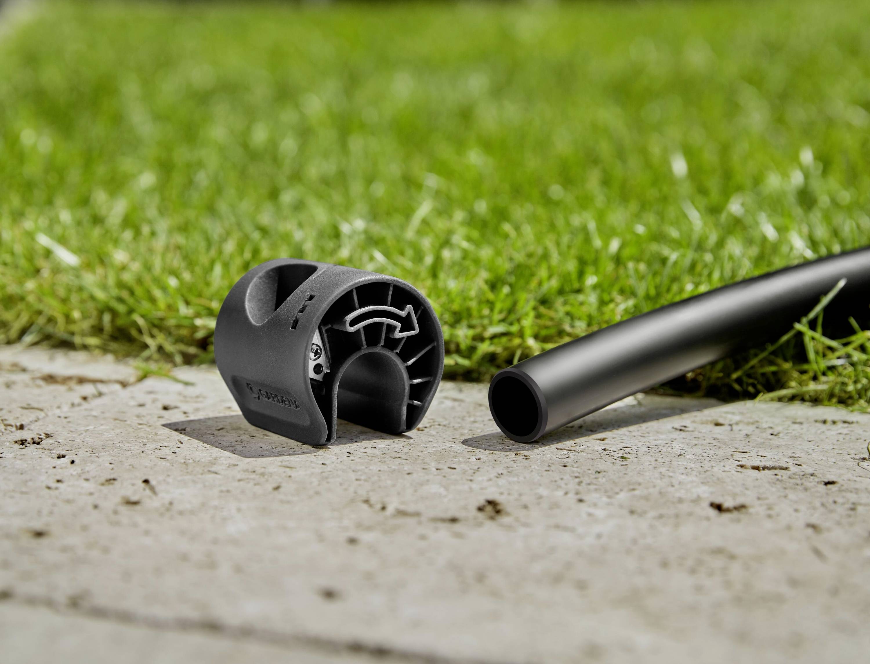 Eine Schlauchtrommel und ein Gartenschlauch liegen auf einem gepflasterten Weg vor einer Rasenfläche.