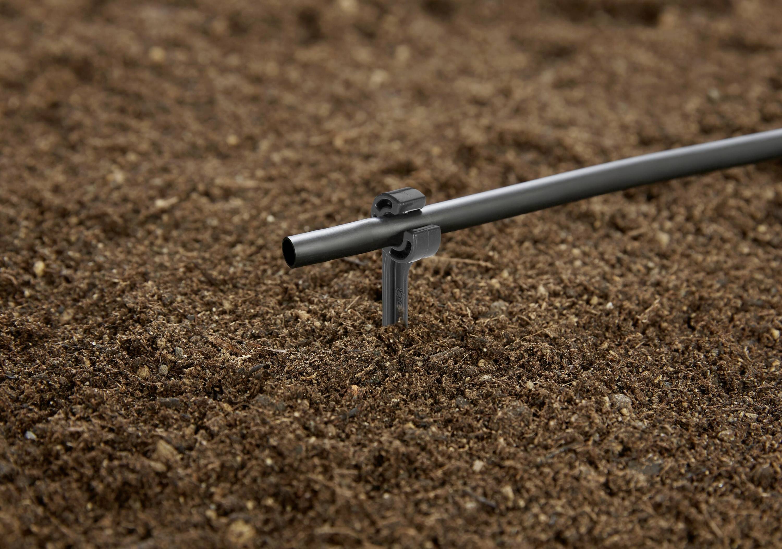 Ein Bewässerungsrohr steht in einem mit Erde bedeckten Gartenbeet.