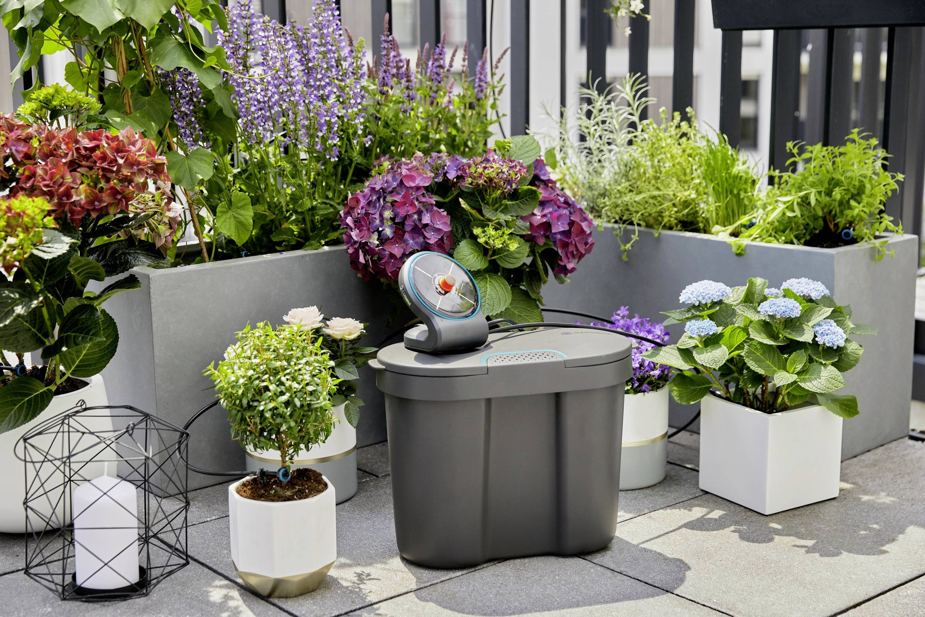 Ein automatisches Bewässerungssystem auf einer Terrasse, umgeben von blühenden Pflanzen in modernen Pflanzgefäßen.
