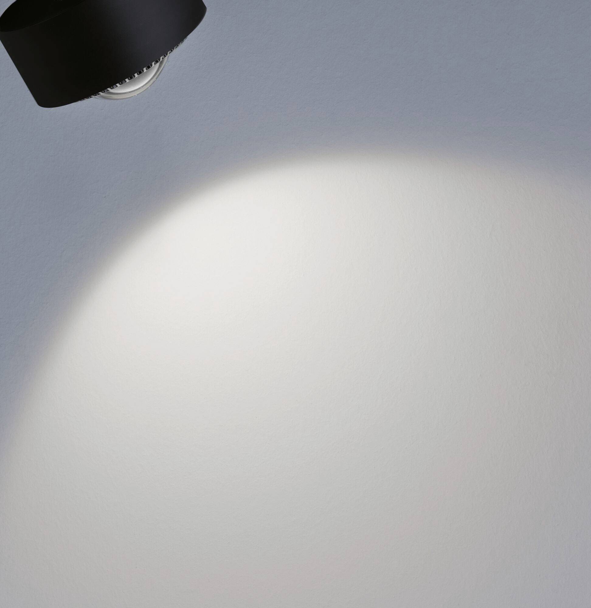 Ein Spotlicht an der Decke beleuchtet einen kreisförmigen Bereich auf einer grauen Wand, der Rest ist im Schatten.