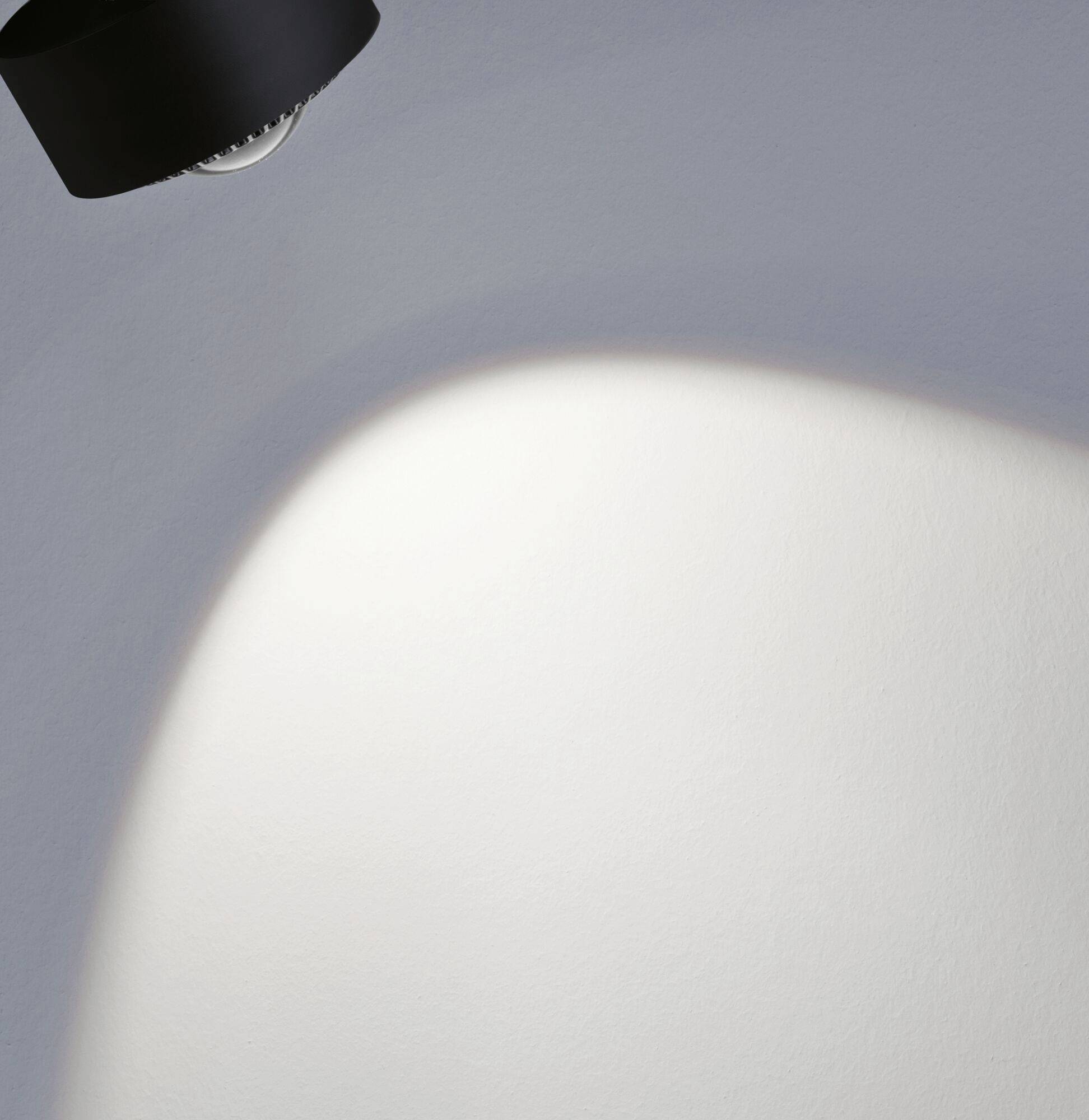 Eine Lampe wirft warmes Licht auf eine weiße, gebogene Fläche und schafft einen sanften Übergang von Licht zu Schatten.