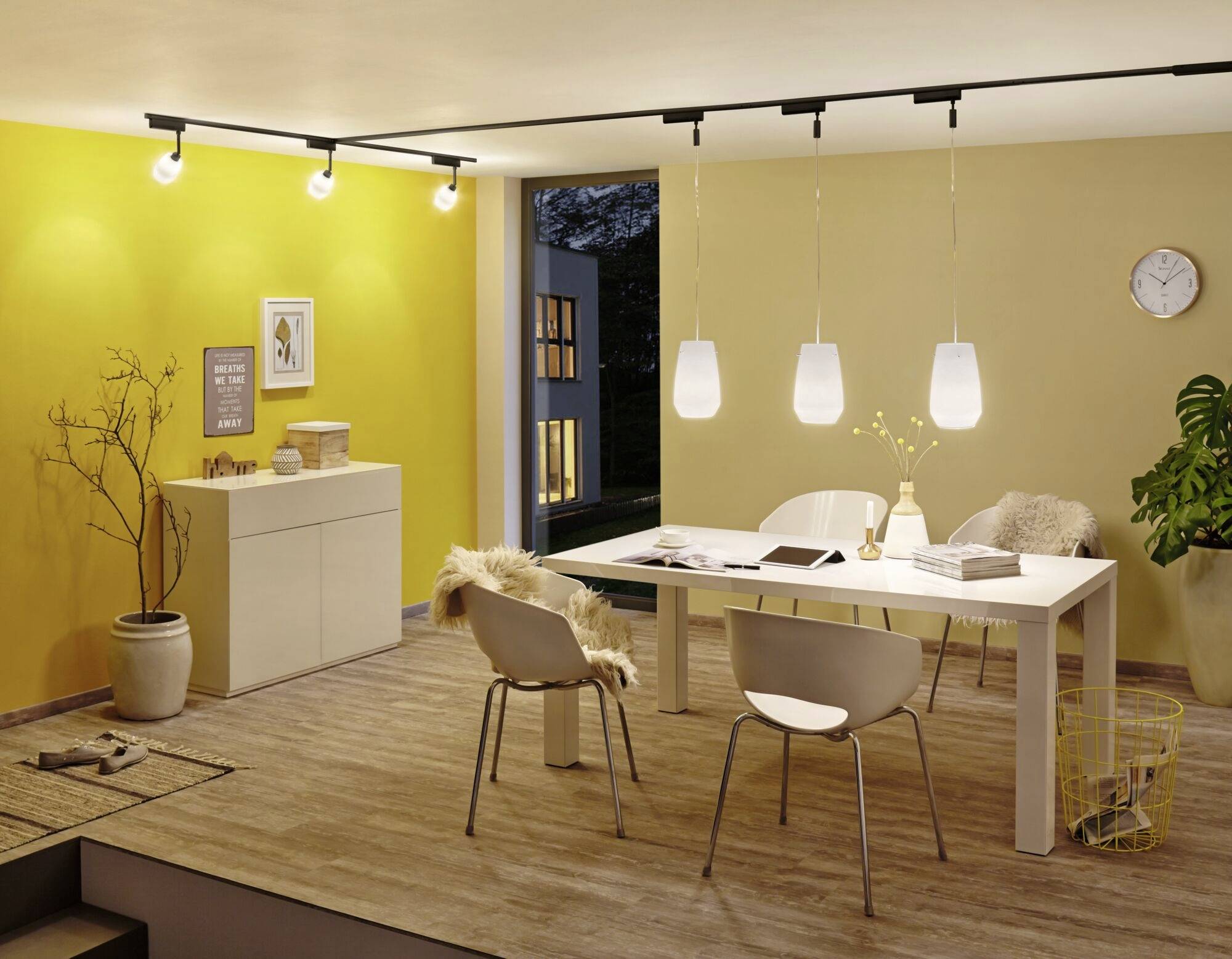 Ein modernes Wohnzimmer mit gelben Wänden, einem weißen Tisch mit vier Stühlen, Hängelampen und einer geöffneten Glastür zu einem Balkon.