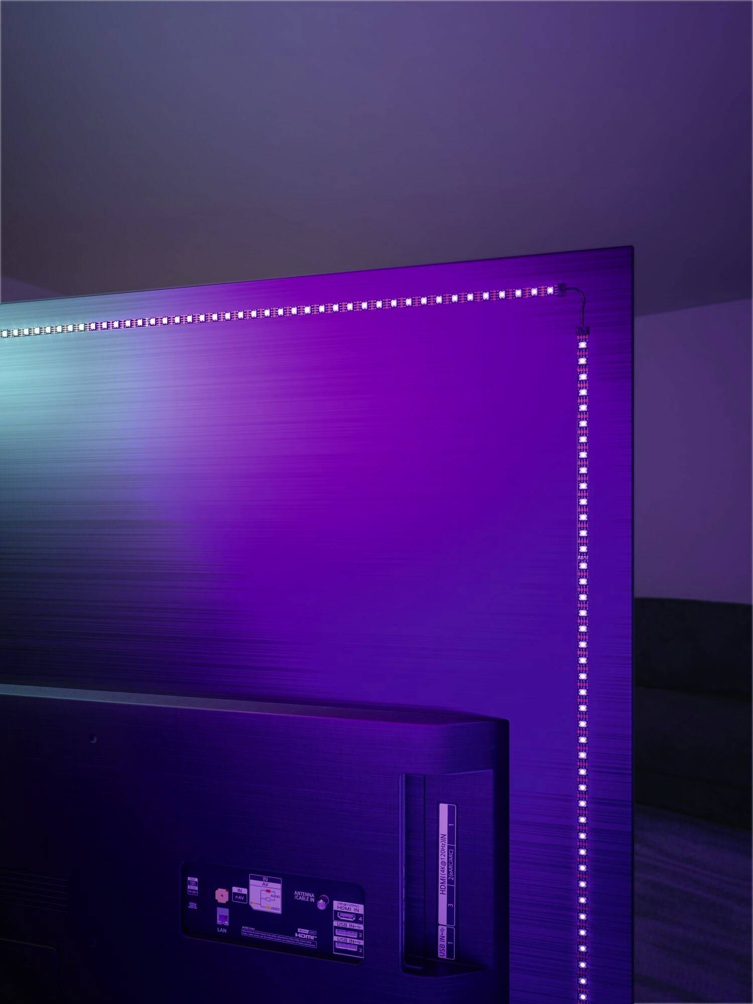 Ein Fernseher mit LED-Hintergrundbeleuchtung in Lila- und Blautönen an der Wand montiert. Die LED-Leiste verläuft entlang der Kante.