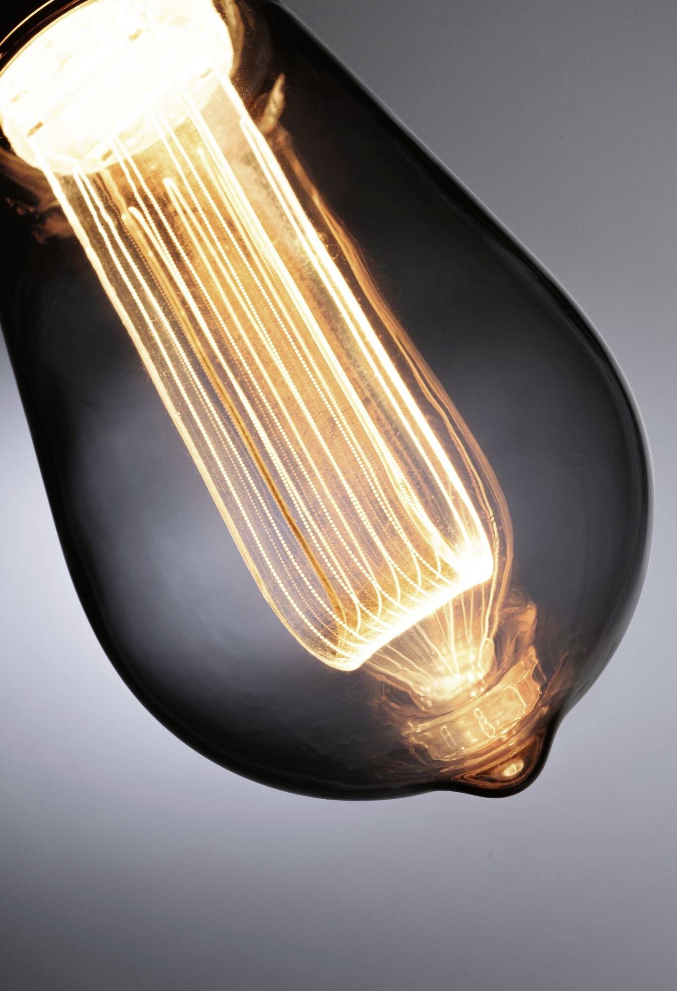 Glühbirne mit sichtbarem Glühdraht, leuchtet warmes Licht aus, in einer dunklen Umgebung aufgenommen.