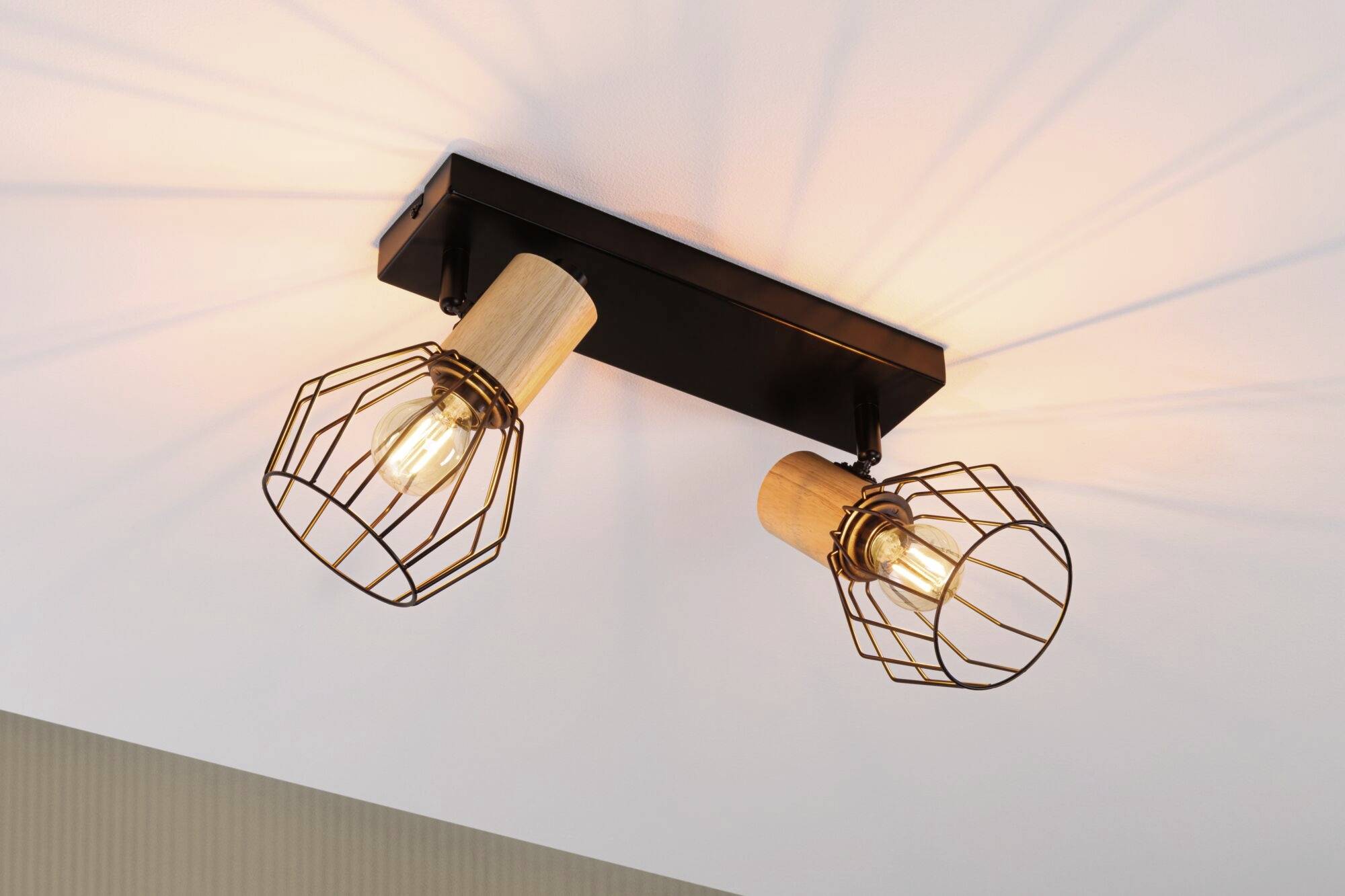 Zwei Deckenleuchten mit Holzhalterungen und Metallgitterschirmen, die warmes Licht in einem modernen Raum ausstrahlen.