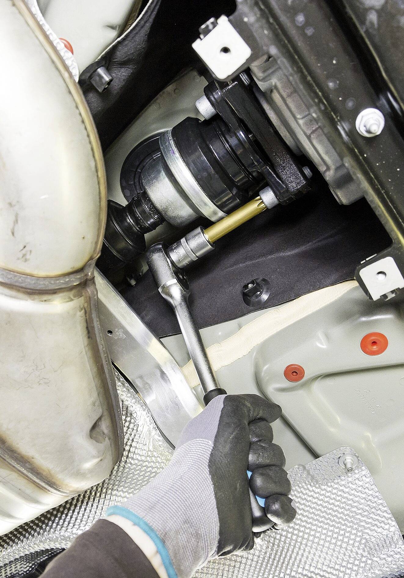 Eine Person zieht eine Schraube an einem Fahrzeugteil mit einem Schraubenschlüssel fest. Das Bild zeigt eine Reparaturszene im Motorraum.