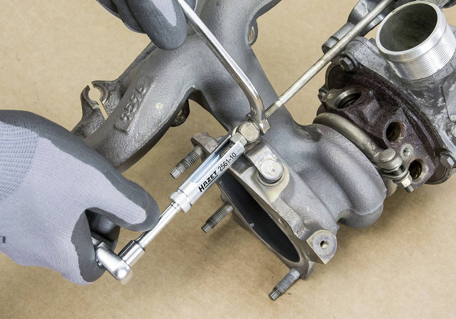 Eine Person mit grauem Handschuh verwendet ein Drehmomentschlüssel, um eine Schraube an einem metallischen Autoteilt zu bearbeiten.