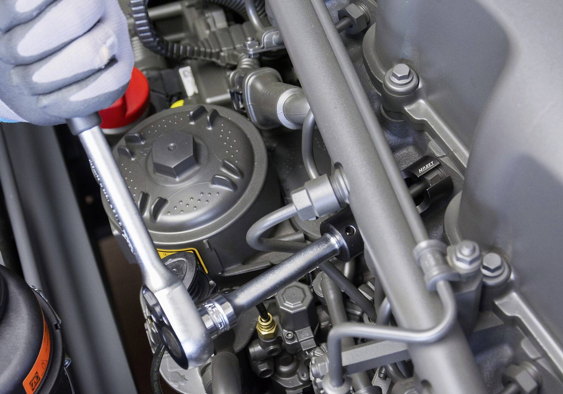 Nahaufnahme eines Mechanikers, der eine Ratsche verwendet, um an einem Motorblock zu arbeiten, umgeben von verschiedenen Motorteilen.