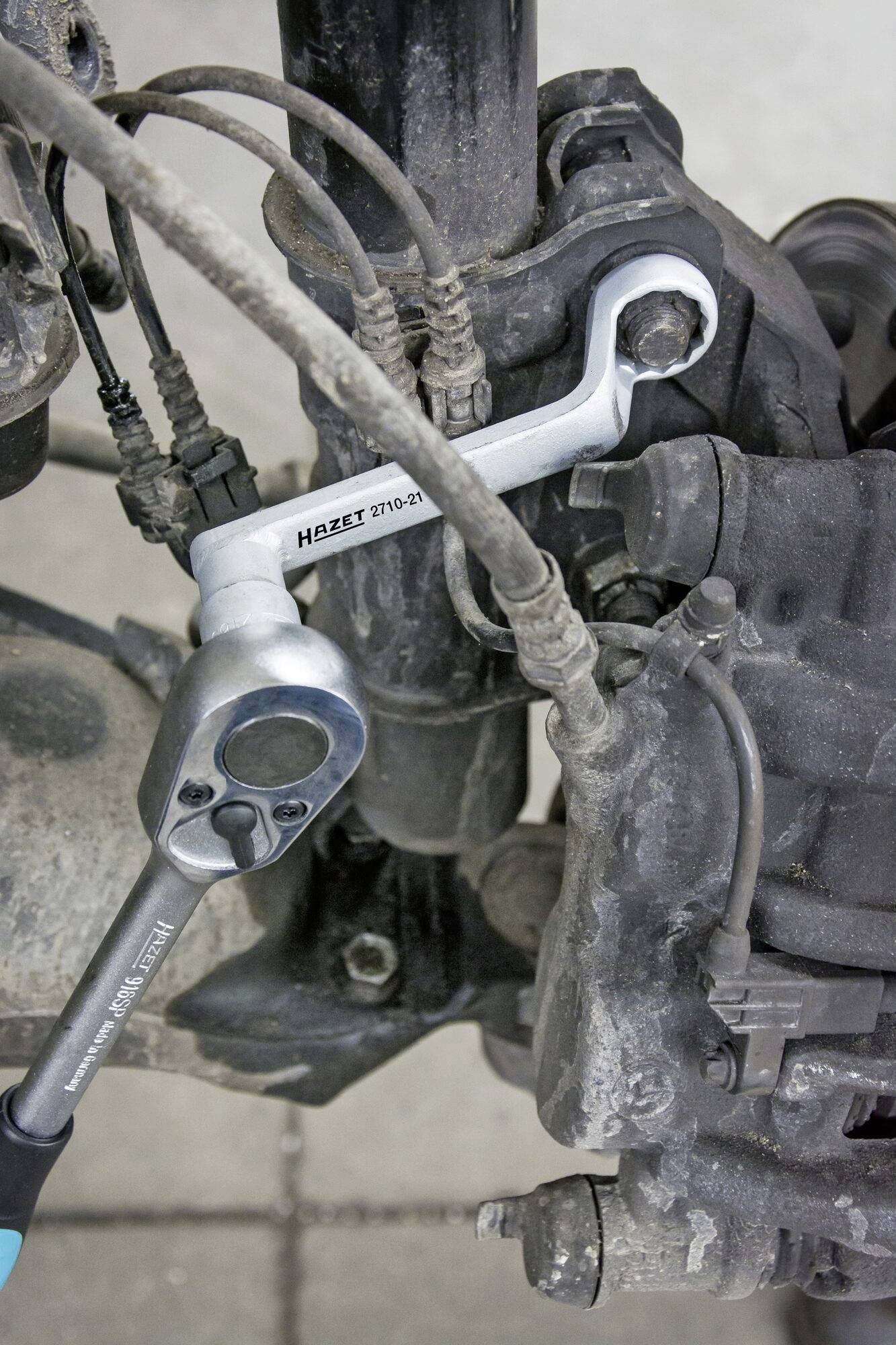 Ein Mechaniker arbeitet an einer Autoaufhängung, verwendet einen Schraubenschlüssel und eine Ratsche zur Reparatur.