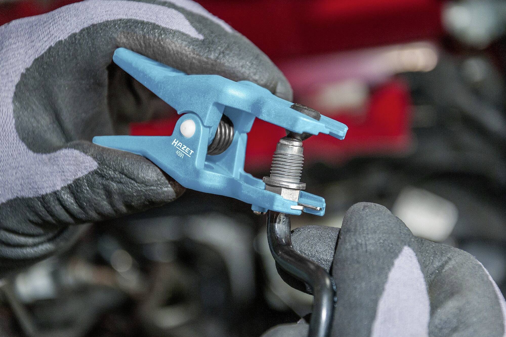 Nahaufnahme von Händen in Handschuhen, die ein blaues Werkzeug halten und eine Zündkerze ausbauen. Hintergrund unscharf, Fokus auf dem Werkzeug.