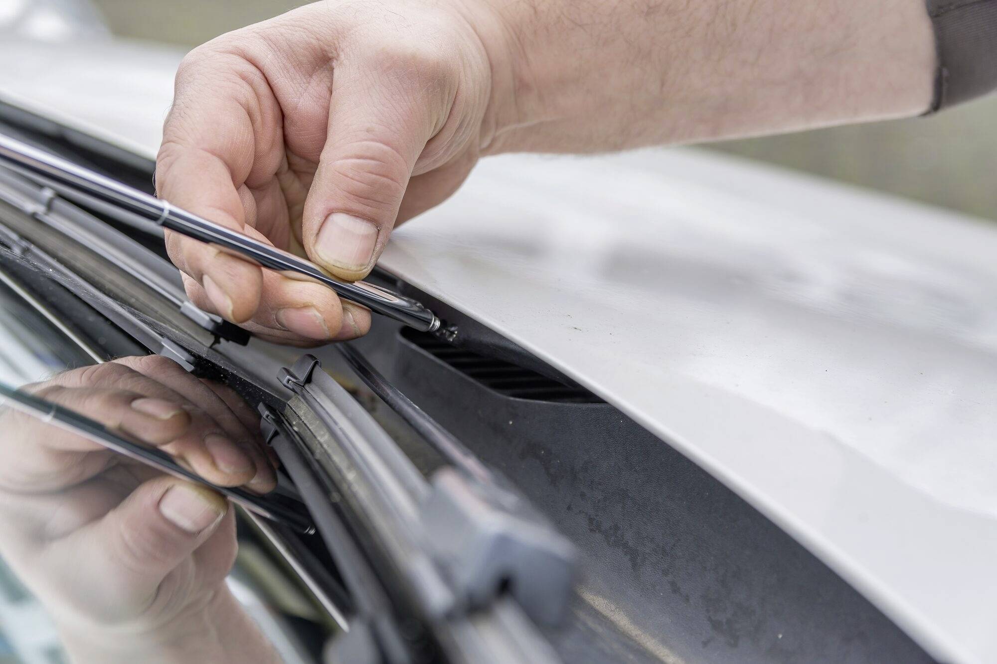 Eine Person wechselt einen Scheibenwischer an einem Auto.