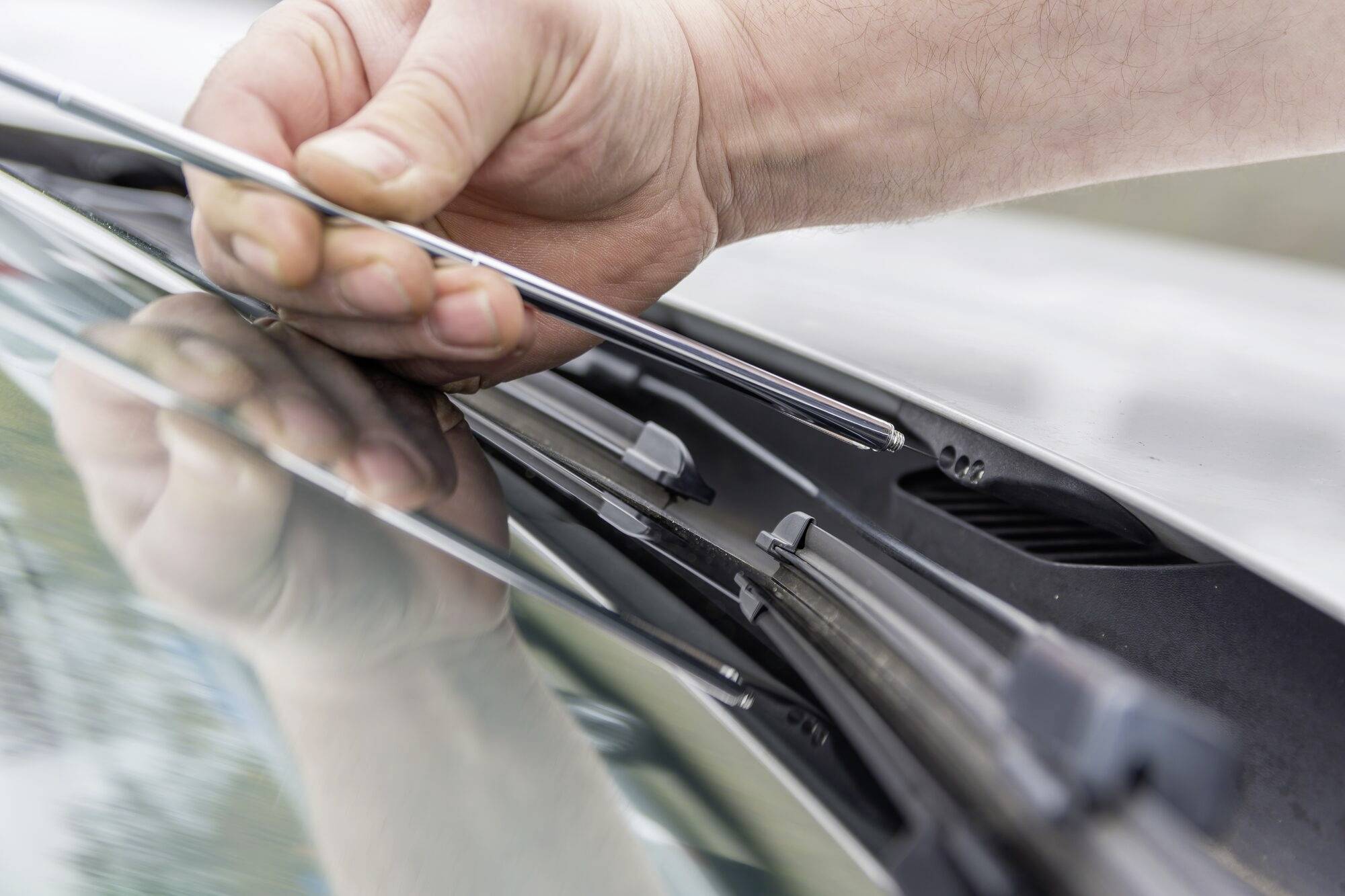 Eine Hand tauscht einen Scheibenwischer an einem Auto aus. Nahaufnahme zeigt das Einsetzen des Wischerblatts in die Halterung.